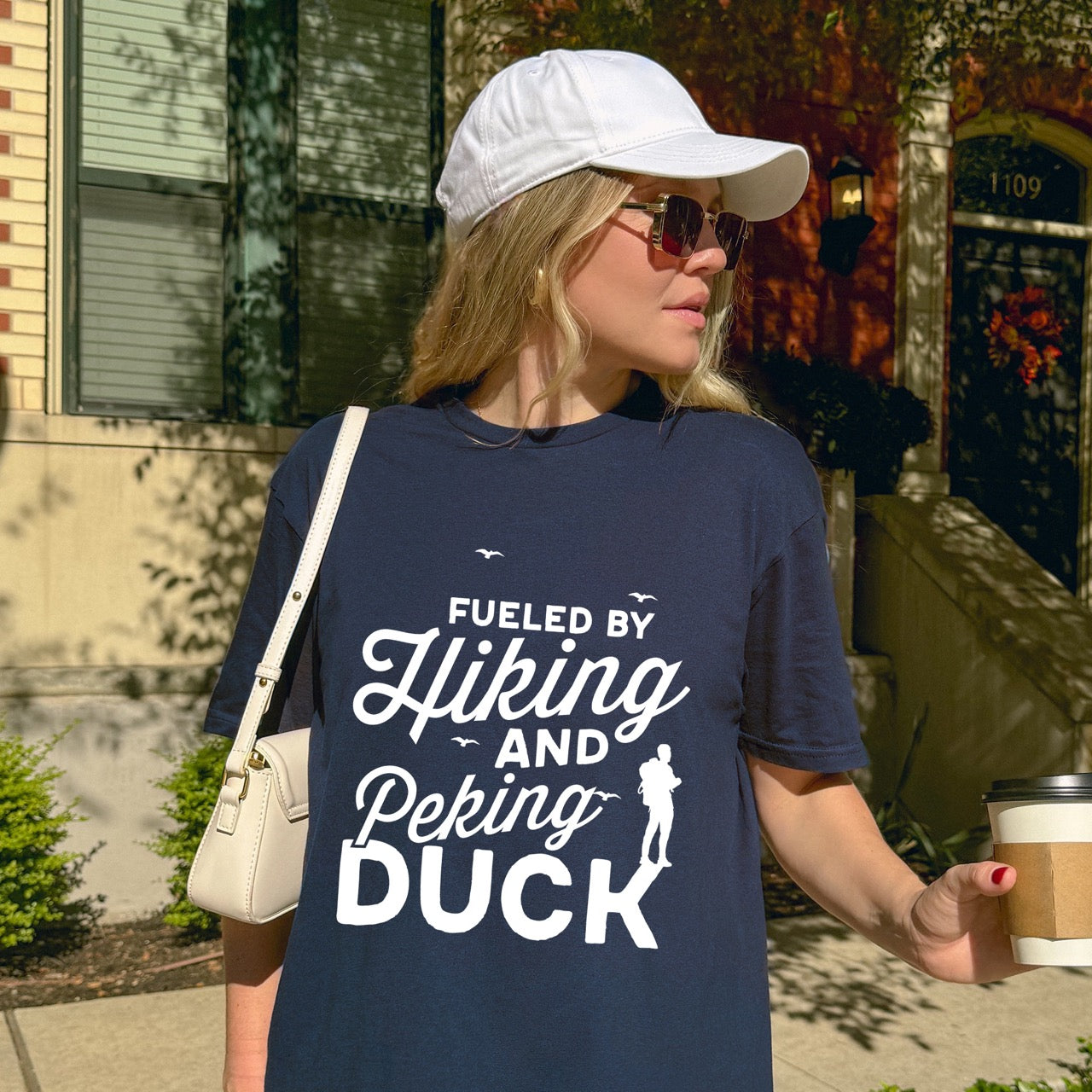 woman wearing Navy Fueled by Hiking and Peking Duck statement tee with bold and script typography, flying birds, and hiker silhouette for Chinese food-loving outdoor enthusiasts, hikers and foodies