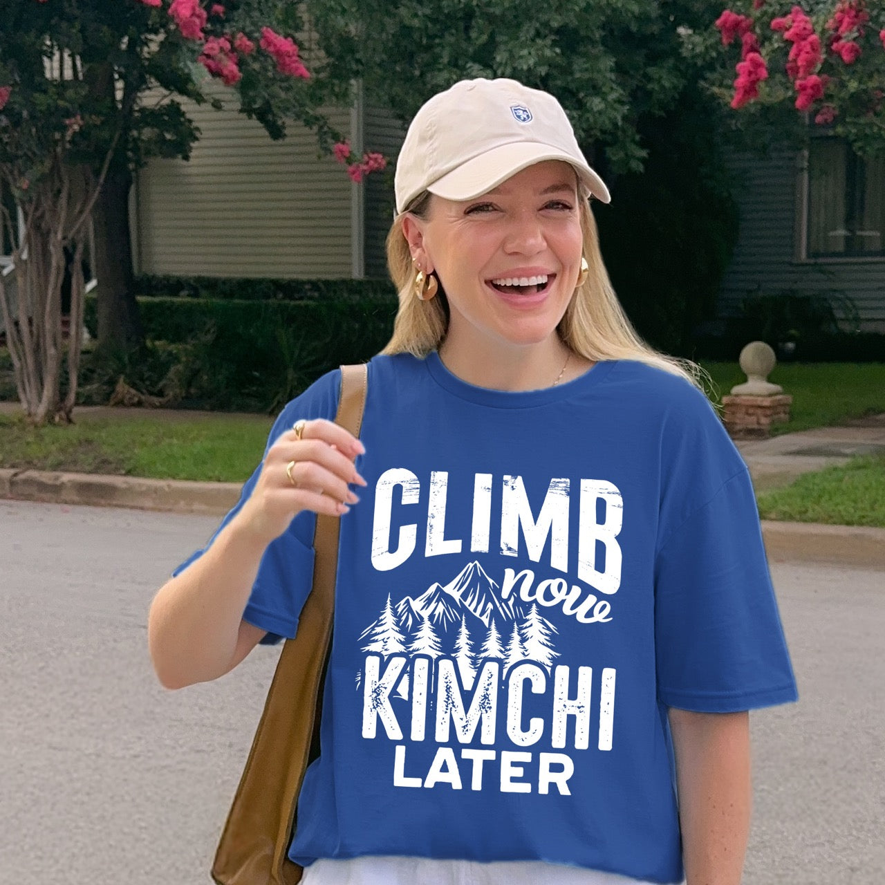 woman wearing Royal blue Climb now Kimchi later statement tee with distressed bold typography, script lettering, mountain peaks, and pine trees for Korean food-loving climbers, hikers and foodies.