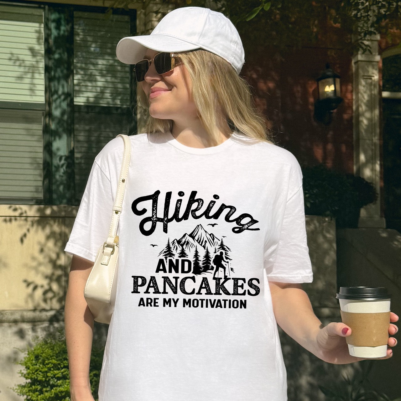 Wearing white Blue Hiking and Pancakes are my motivation statement tee with flowing script typography, bold lettering, mountain peaks, pine trees, hiker silhouette, and flying birds for pancake-loving outdoor enthusiasts, hikers and foodies