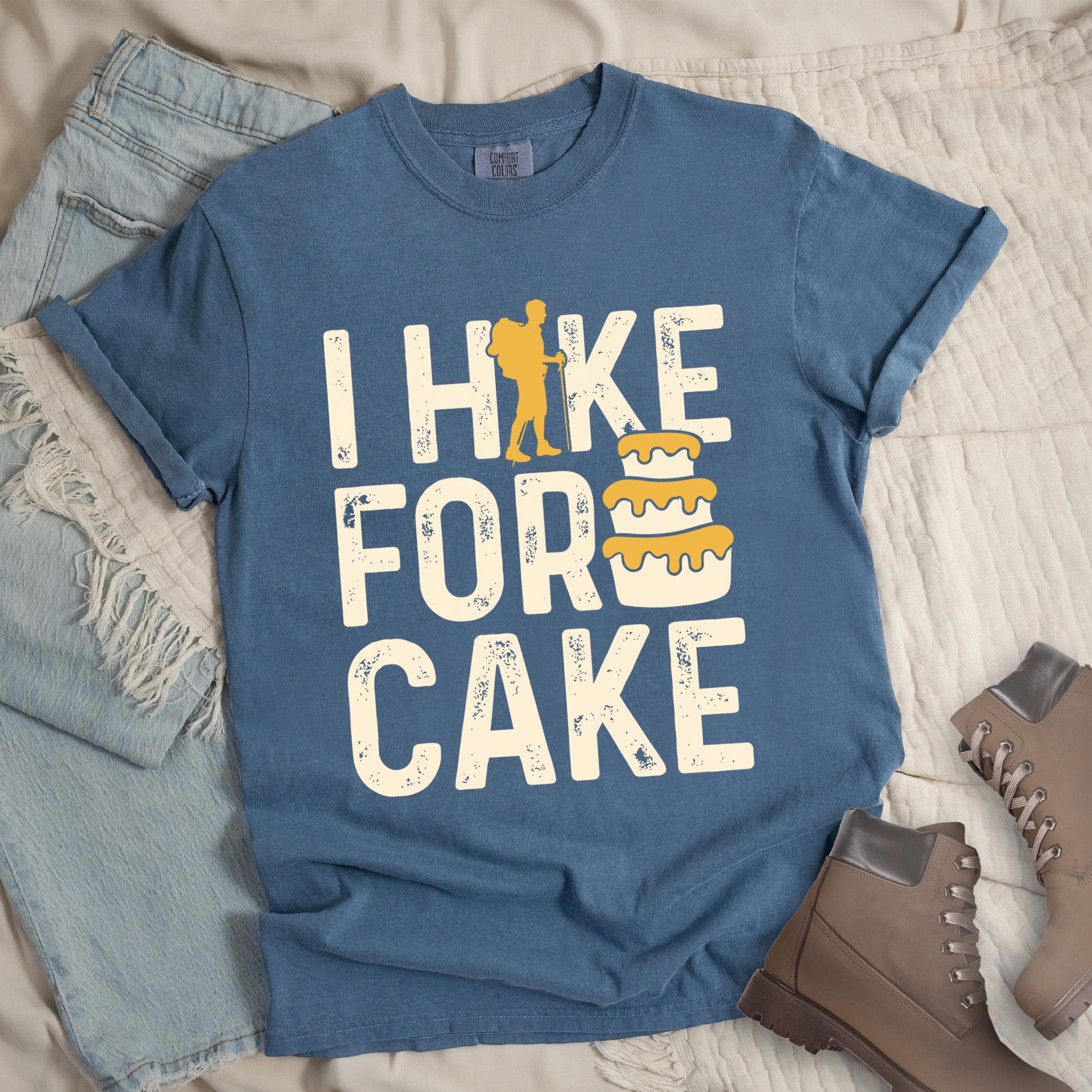Dark blue shirt with the bold text “I Hike for Cake” and an illustration of a layered cake with frosting - I Hike for Cake vintage statement tee with distressed typography, hiker silhouette, and layered cake illustration on Comfort Colors shirt for dessert-loving outdoor enthusiasts.