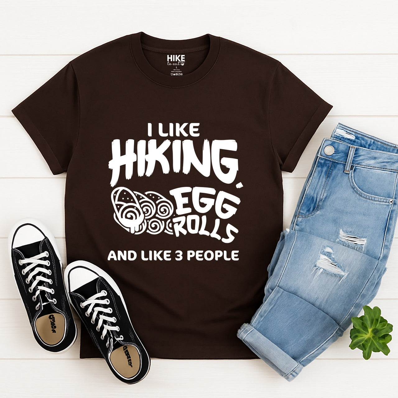 Dark Chocolate Brown I like Hiking, Egg Rolls and like 3 People funny introvert statement tee with bold brushstroke typography and egg roll illustrations for Asian food-loving outdoor enthusiasts, hikers and foodies laid flat with pants and shoes