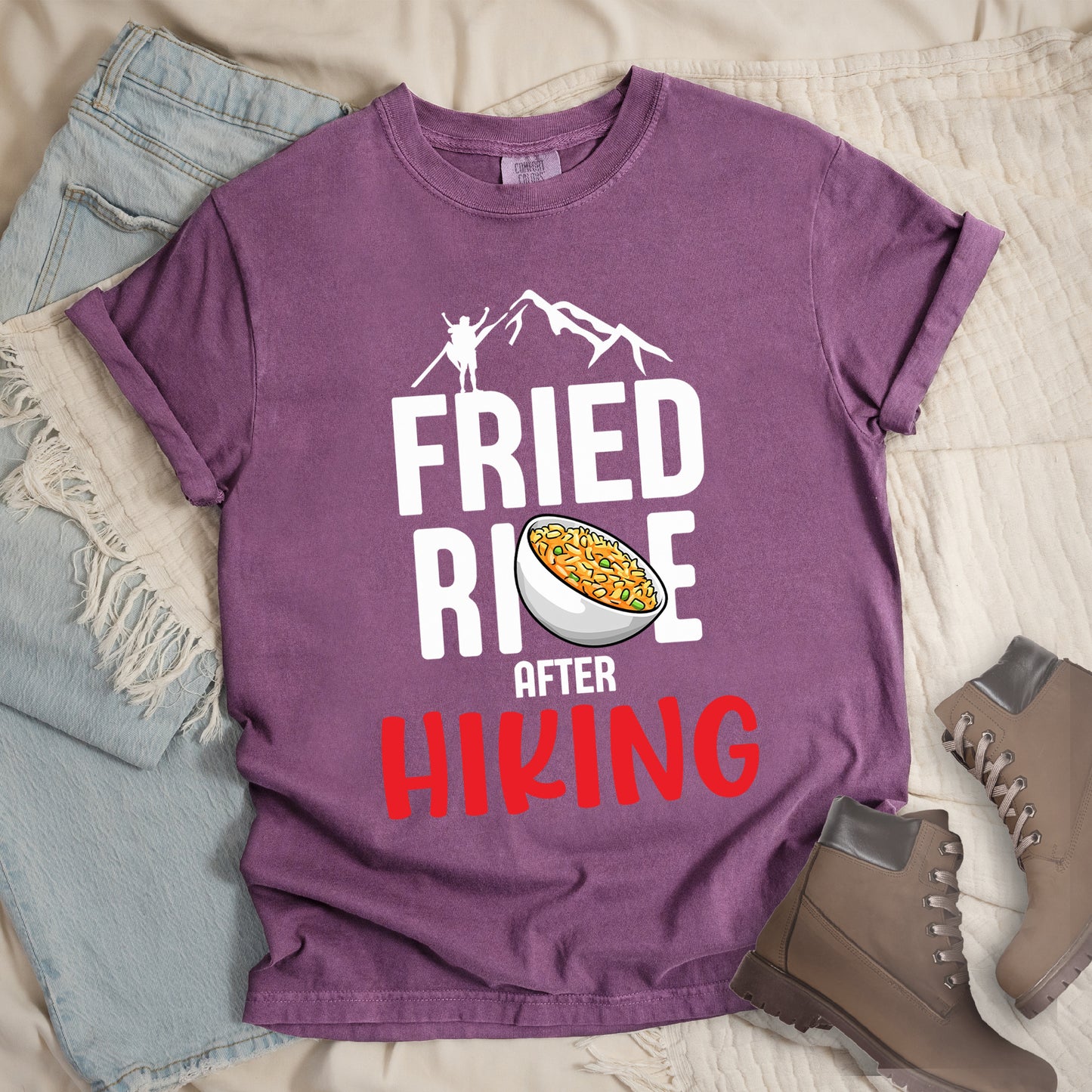 Berry (Dark Violet) t-shirt with text "FRIED RICE AFTER HIKING". The top features white mountain silhouettes with a small hiker figure. "FRIED RICE" appears in large white letters with an illustration of a bowl of fried rice replacing the letter "C" in "RICE", tilted slightly to the right. The word "AFTER" is in small white text, and "HIKING" appears at the bottom in bold red letters.