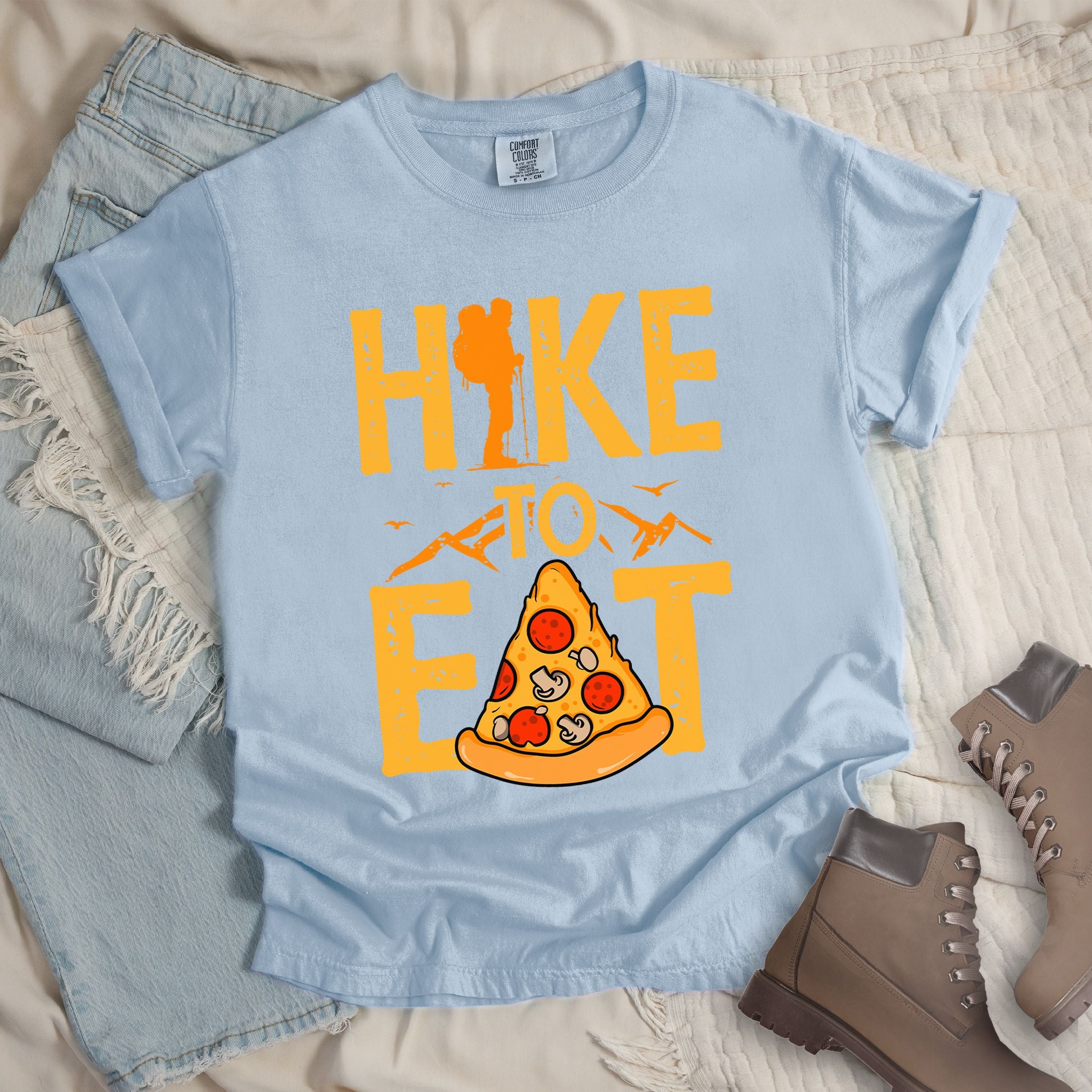 Light blue shirt with a Hiking design of a slice of pizza and shows 'Hike To Eat' phrase in bold text