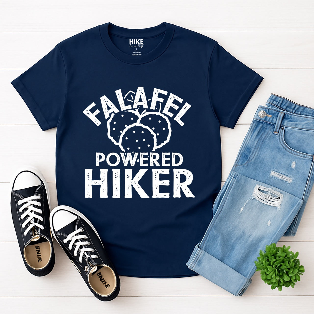 Navy Falafel Powered Hiker statement tee with bold distressed curved typography and detailed falafel illustration for Middle Eastern food-loving outdoor enthusiasts, foodies and hikers laid flat with shoes and pants