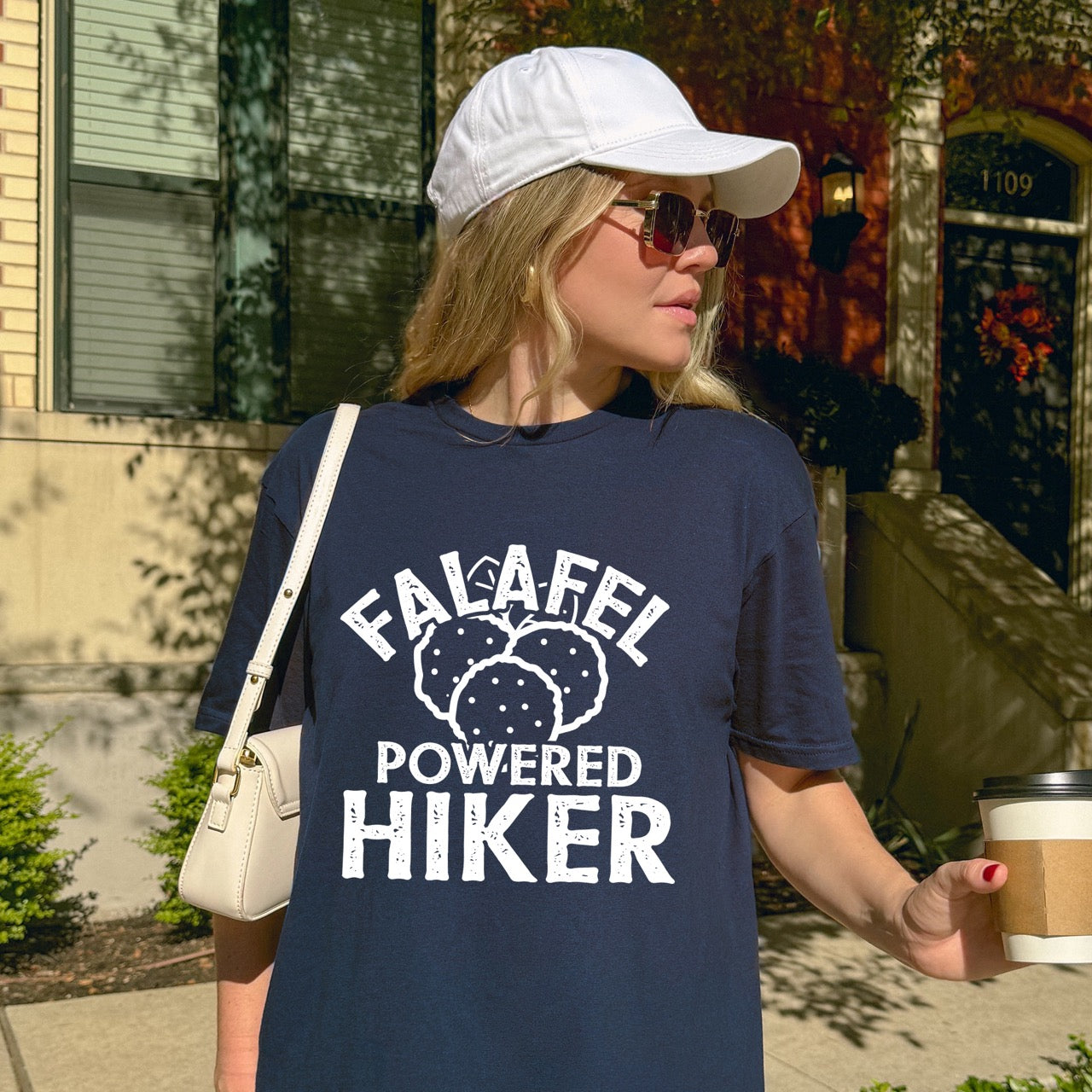 Woman wearing Navy Falafel Powered Hiker statement tee with bold distressed curved typography and detailed falafel illustration for Middle Eastern food-loving outdoor enthusiasts, foodies and hikers