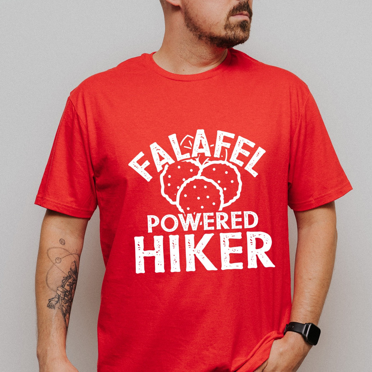 Man wearing Red Falafel Powered Hiker statement tee with bold distressed curved typography and detailed falafel illustration for Middle Eastern food-loving outdoor enthusiasts, foodies and hikers