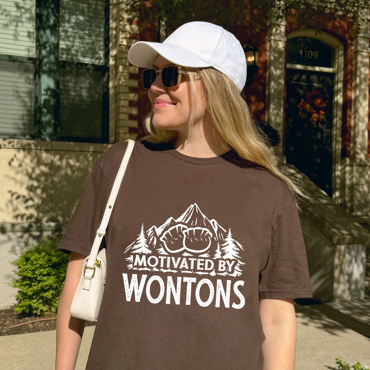 Woman wearing Dark chocolate Motivated by Wontons statement tee with bold distressed typography, mountain peaks, pine trees, and wonton illustration for Chinese food-loving outdoor enthusiasts, hikers and foodies