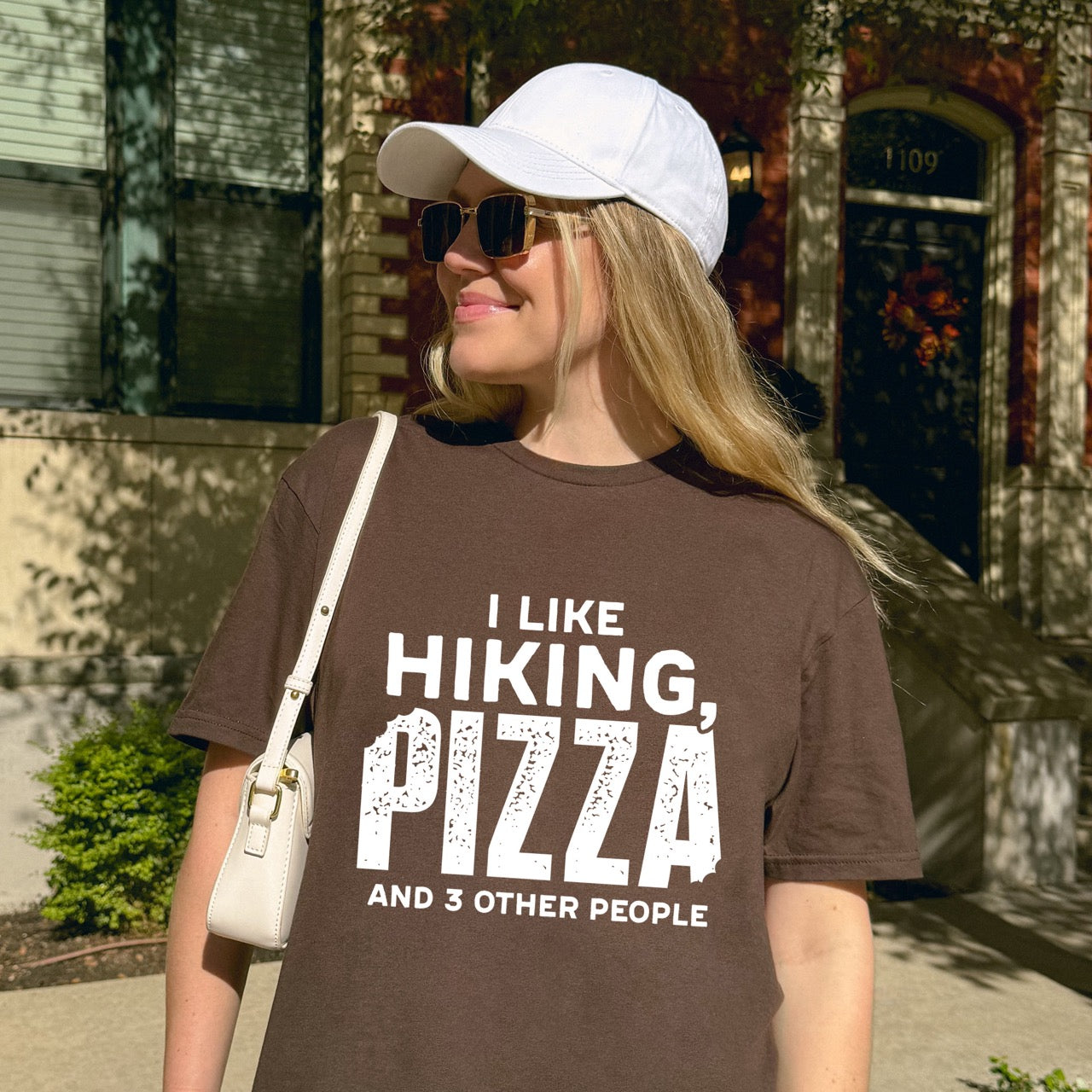 Woman wearing Dark Chocolate Motivated by Wontons statement tee with bold distressed typography, mountain peaks, pine trees, and wonton illustration for Chinese food-loving outdoor enthusiasts, hikers and foodies