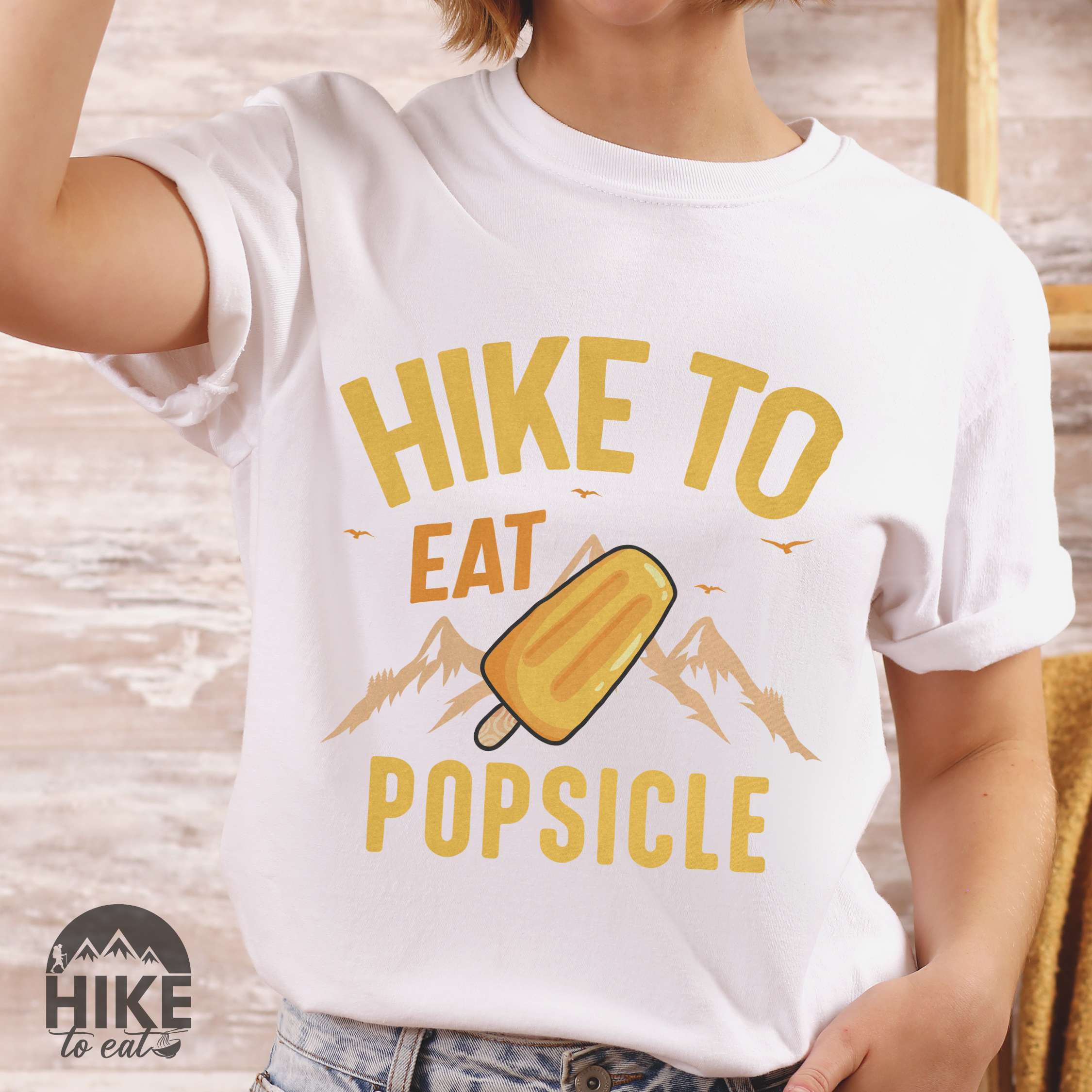 Woman wearing white "Hike to Eat Popsicle" colored vintage tee with bold typography, mountains, illustrated flavored popsicle, and backpackers with a sweet tooth.