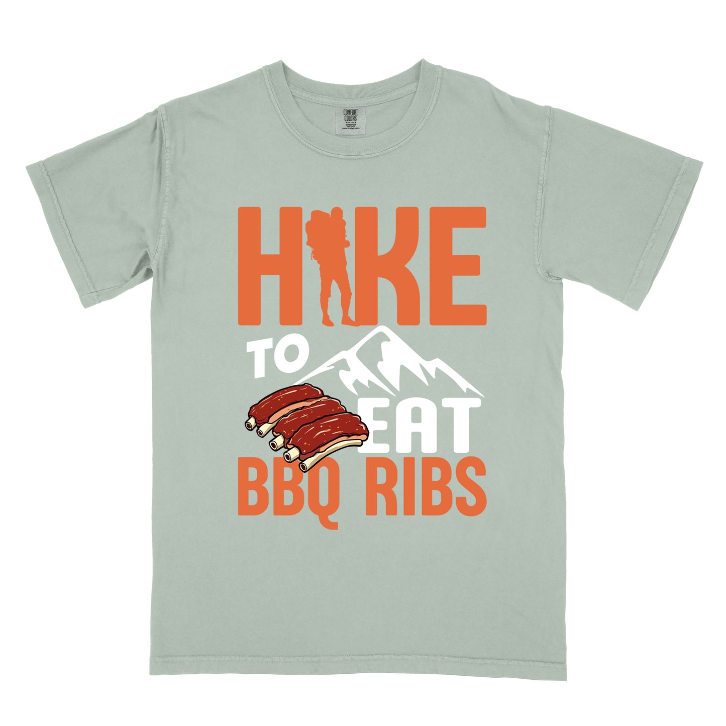 Bay (Light Gray) t-shirt with text "HIKE TO EAT BBQ RIBS". The word "HIKE" appears in orange with a hiker silhouette replacing the "I". Below that is "TO" in white text above a white mountain graphic. "EAT" appears in white, and "BBQ RIBS" in orange at the bottom. Between "EAT" and "BBQ RIBS" is an illustration of a rack of barbecue ribs with exposed bones.