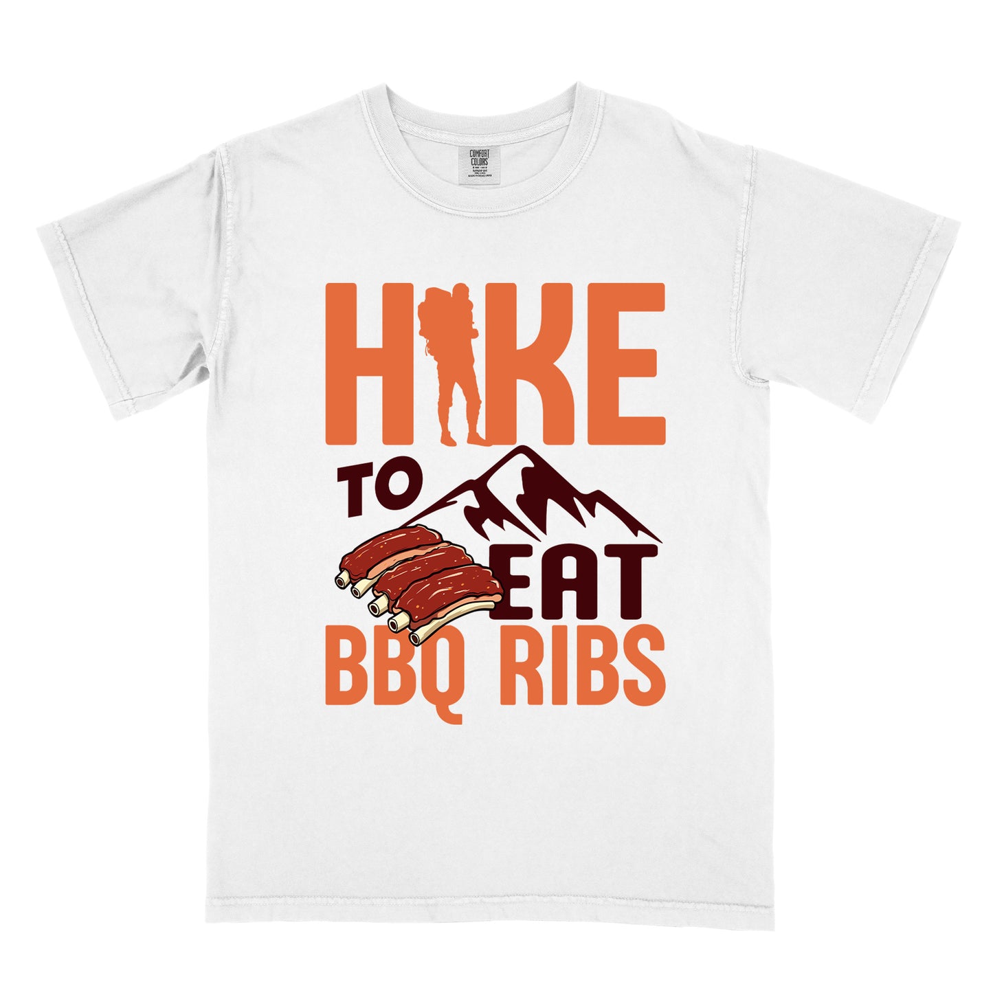 White t-shirt with text "HIKE TO EAT BBQ RIBS". The word "HIKE" appears in orange with a hiker silhouette replacing the "I". Below that is "TO" in deep brown-red text above a deep brown-red mountain graphic. "EAT" appears in deep brown-red, and "BBQ RIBS" in orange at the bottom. Between "EAT" and "BBQ RIBS" is an illustration of a rack of barbecue ribs with exposed bones.