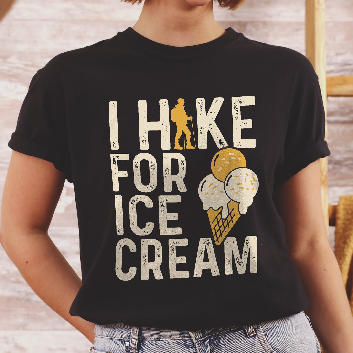 Black graphic t-shirt with 'I Hike for Ice Cream' text in cream lettering featuring orange hiker silhouette and vanilla and mango ice cream cone illustration with waffle cone.
