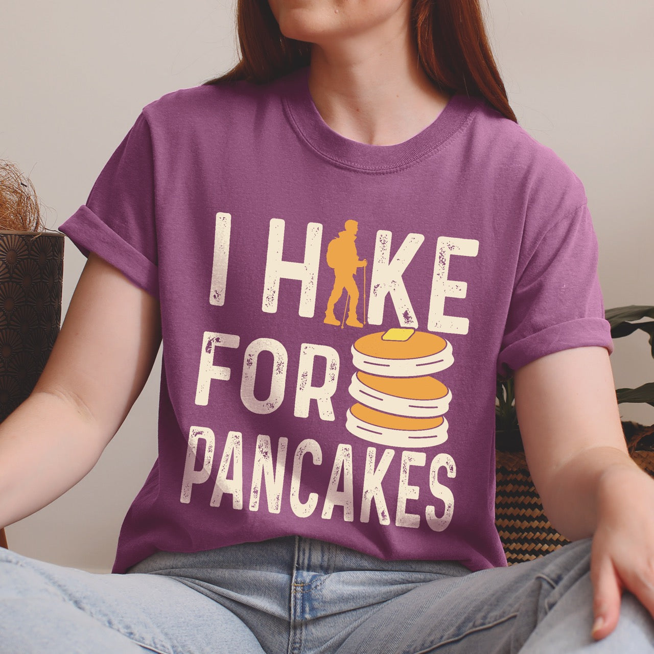 Woman wearing Berry (purple) colored Pancake breakfast lover vintage tee I Hike for Pancakes with distressed cream typography character silhouette with trekking pole and illustrated stacked pancakes with butter on Comfort Colors shirt for brunch and food enthusiasts, hikers and foodies.