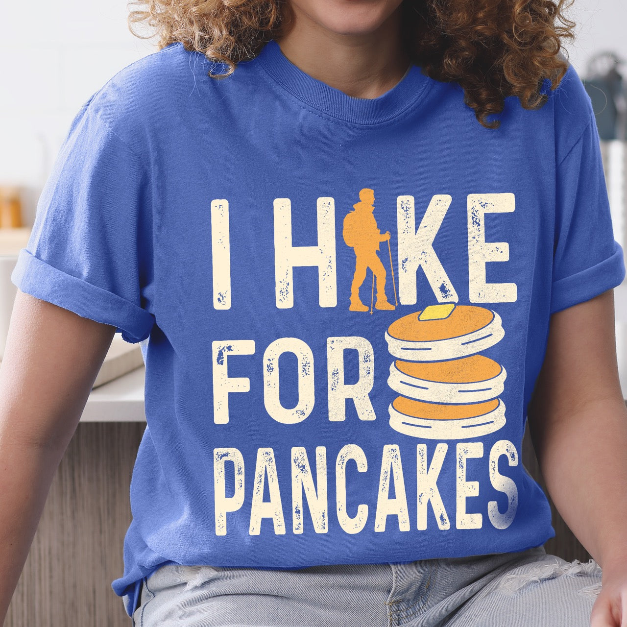 Woman wearing Flo Blue colored Pancake breakfast lover vintage tee I Hike for Pancakes with distressed cream typography character silhouette with trekking pole and illustrated stacked pancakes with butter on Comfort Colors shirt for brunch and food enthusiasts, hikers and foodies.