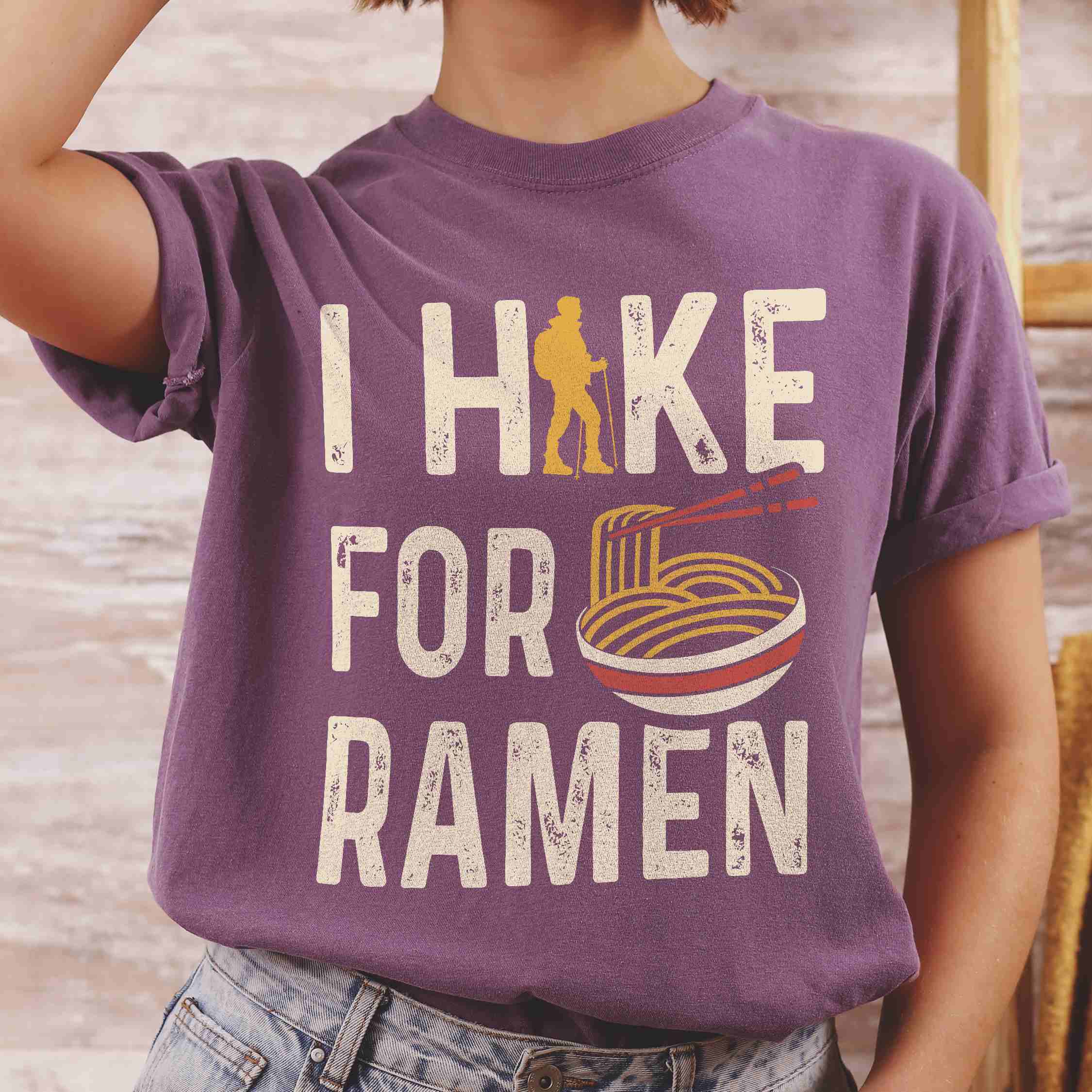 Woman wearing berry colored vintage tee with 'I Hike for Ramen' text in cream lettering, illustrated taco, and backpacker for ramen lovers