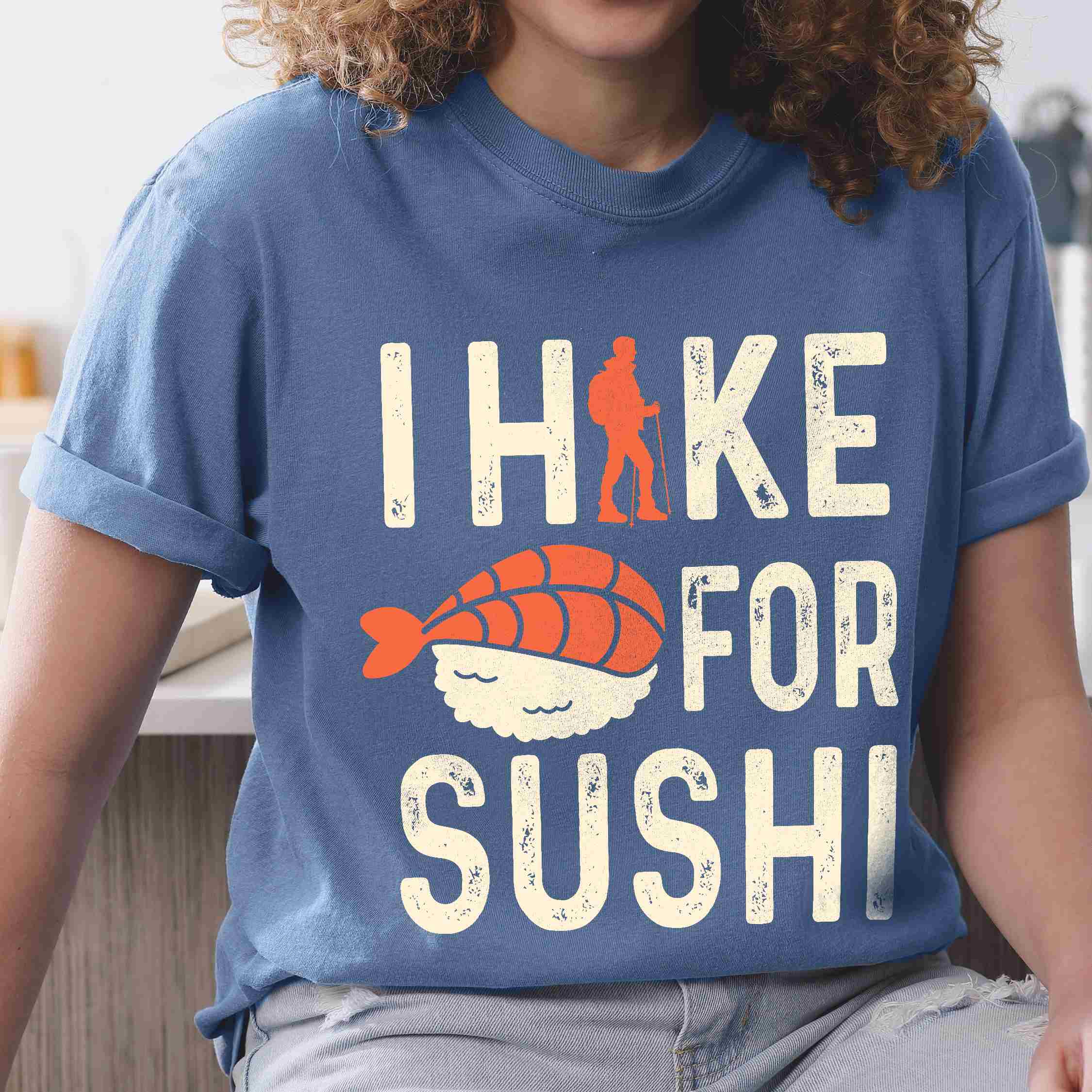 Woman wearing blue jean 'I Hike for Sushi' text in cream lettering, illustrated shrimp sushi, and backpacker for sushi lovers