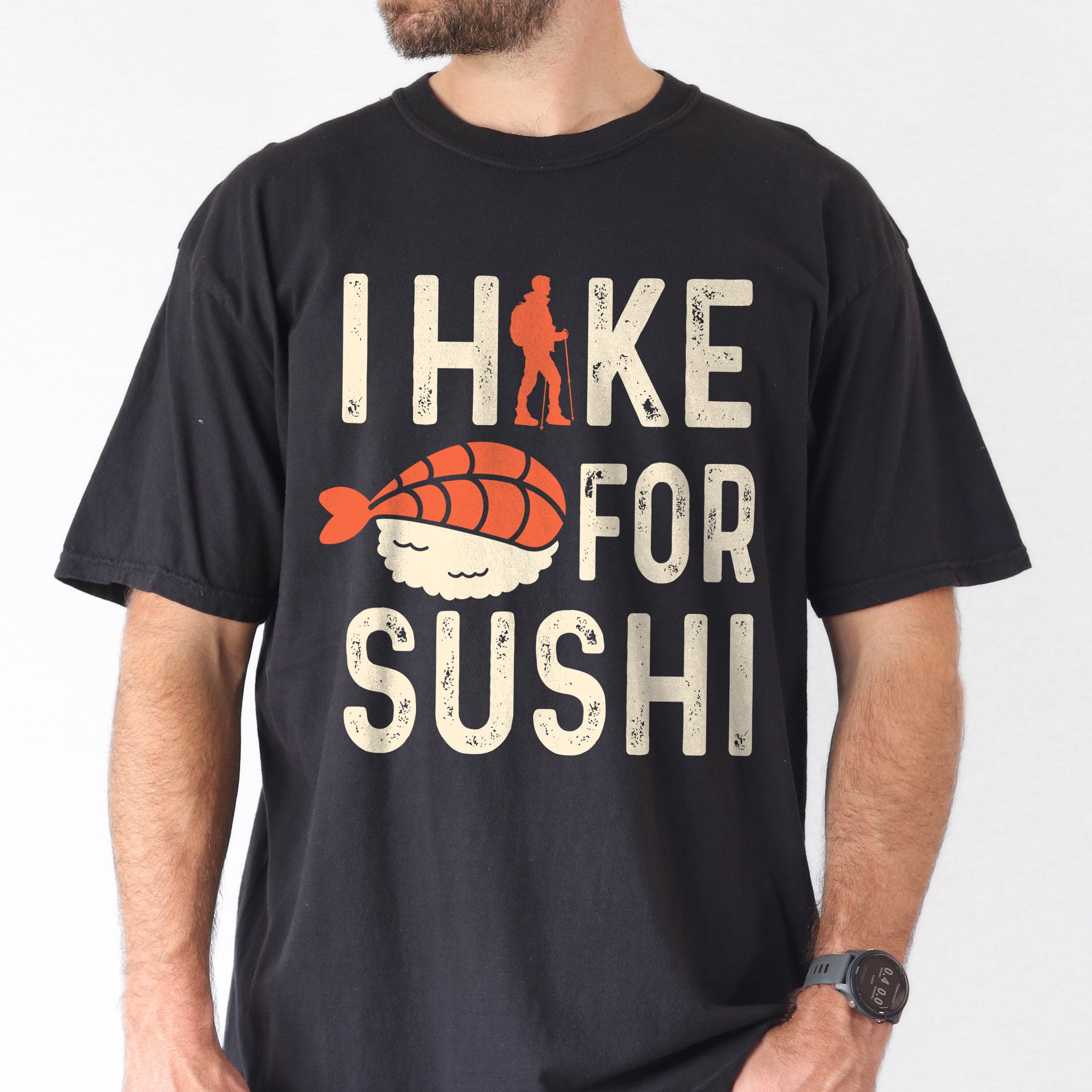 Black graphic t-shirt with 'I Hike for Sushi' text in cream lettering featuring orange hiker silhouette and sushi nigiri illustration with orange fish and white rice