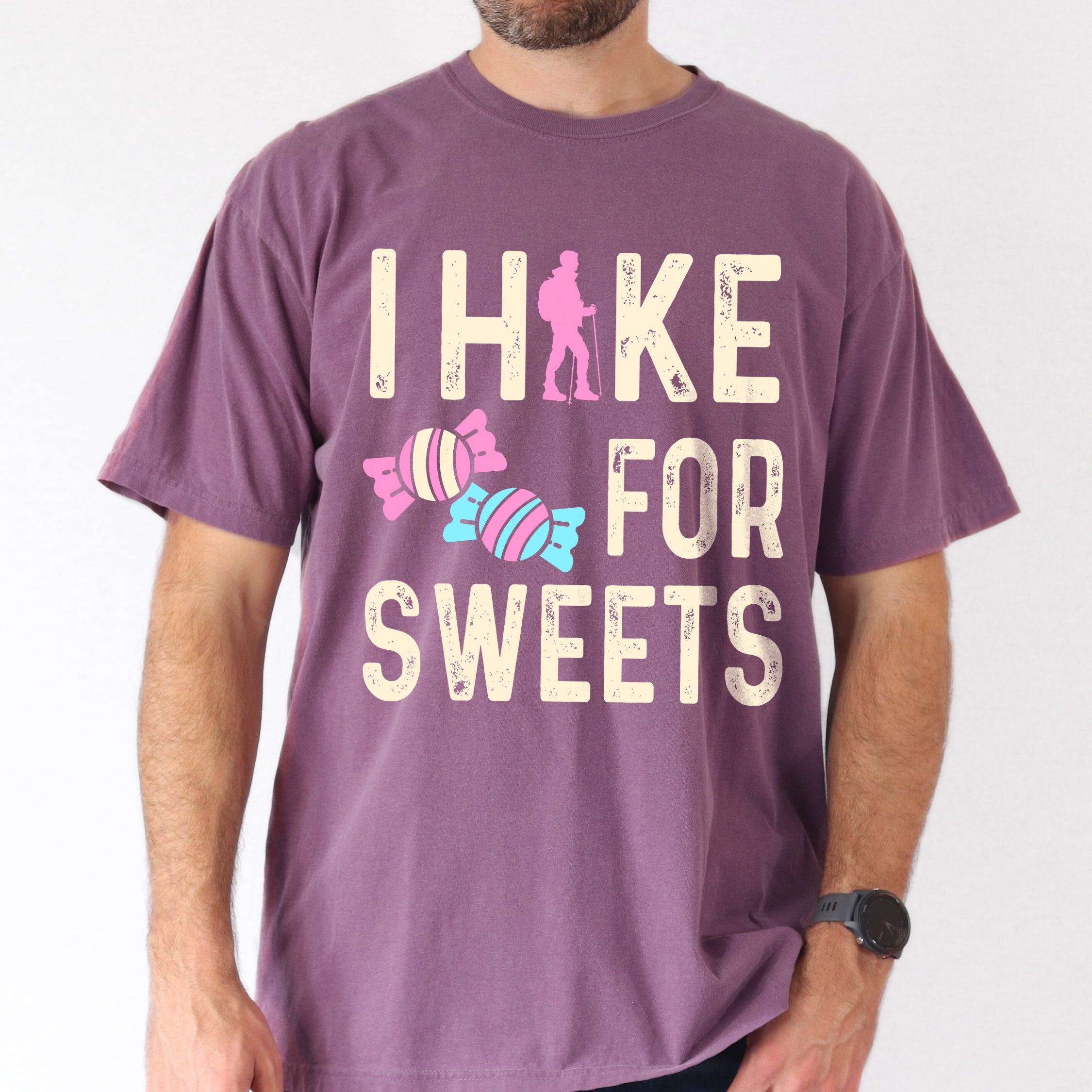 Berry (Dark Violet) graphic t-shirt with 'I Hike for Sweets' text in cream lettering featuring pink hiker silhouette and colorful striped candy illustrations in pink and blue