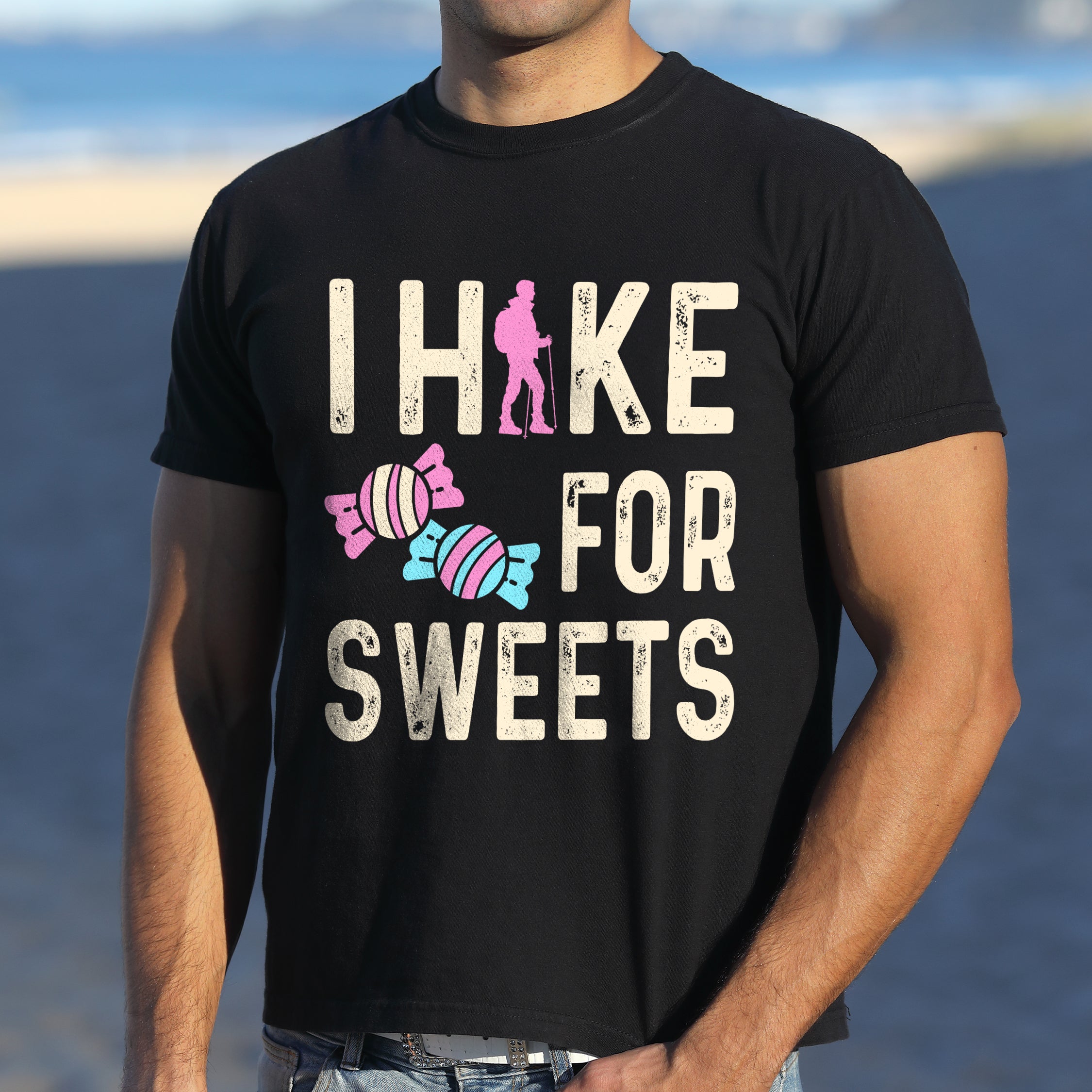 Black graphic t-shirt with 'I Hike for Sweets' text in cream lettering featuring pink hiker silhouette and colorful striped candy illustrations in pink and blue