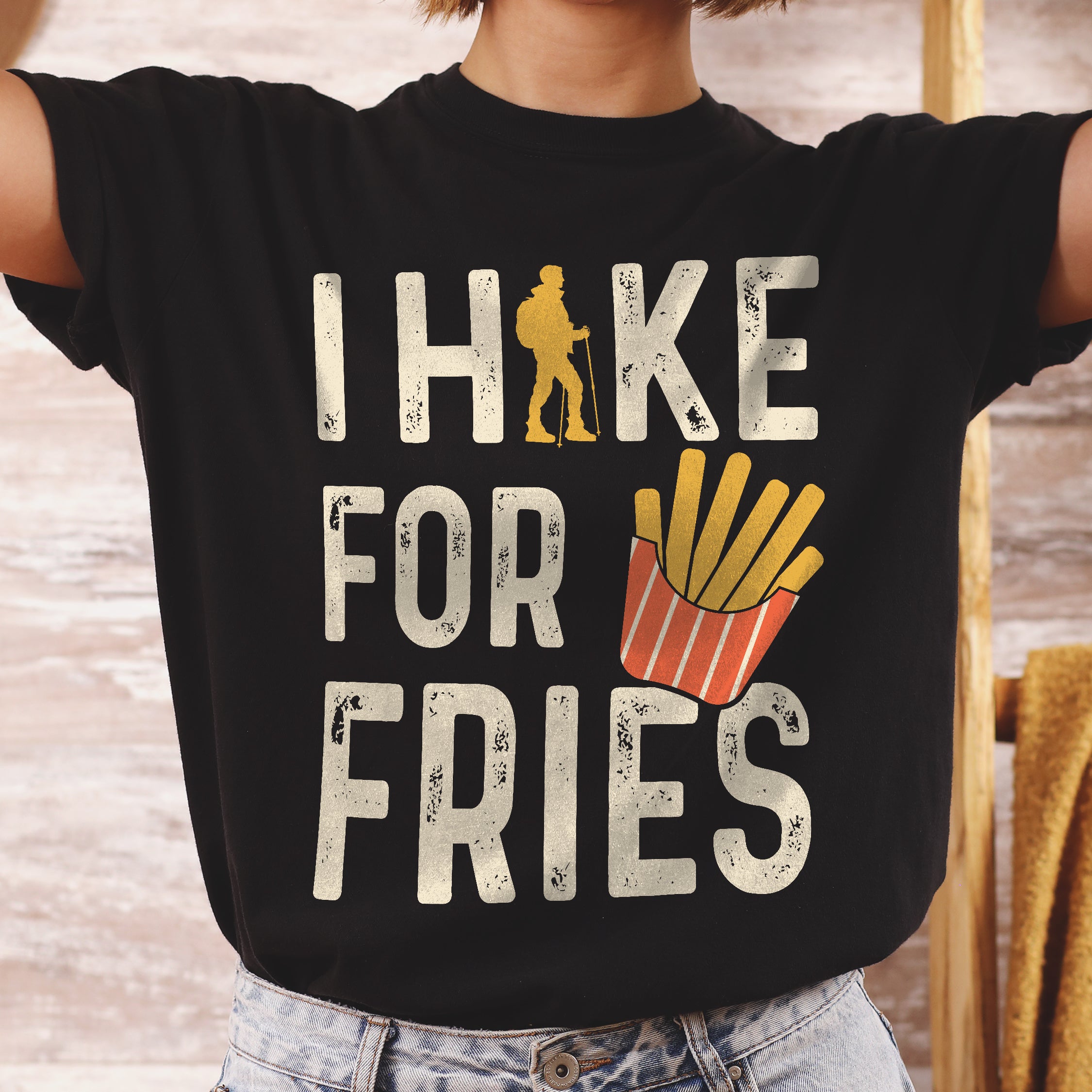 Black graphic t-shirt with 'I Hike for Fries' text in cream lettering featuring yellow hiker silhouette and french fries illustration in red container