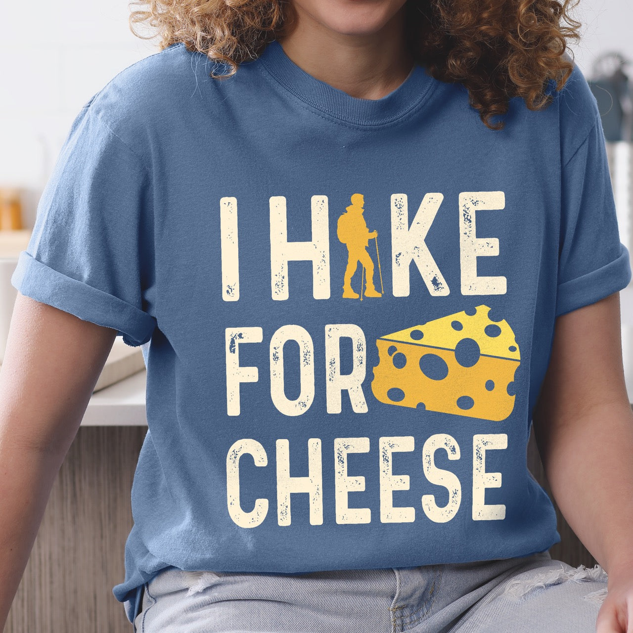 Woman wearing Blue Jean (blue) Cheese lover vintage tee I Hike for Cheese with distressed cream typography character silhouette with trekking pole and illustrated Swiss cheese wedge with holes on Comfort Colors shirt for dairy and food enthusiasts, hikers and foodies.