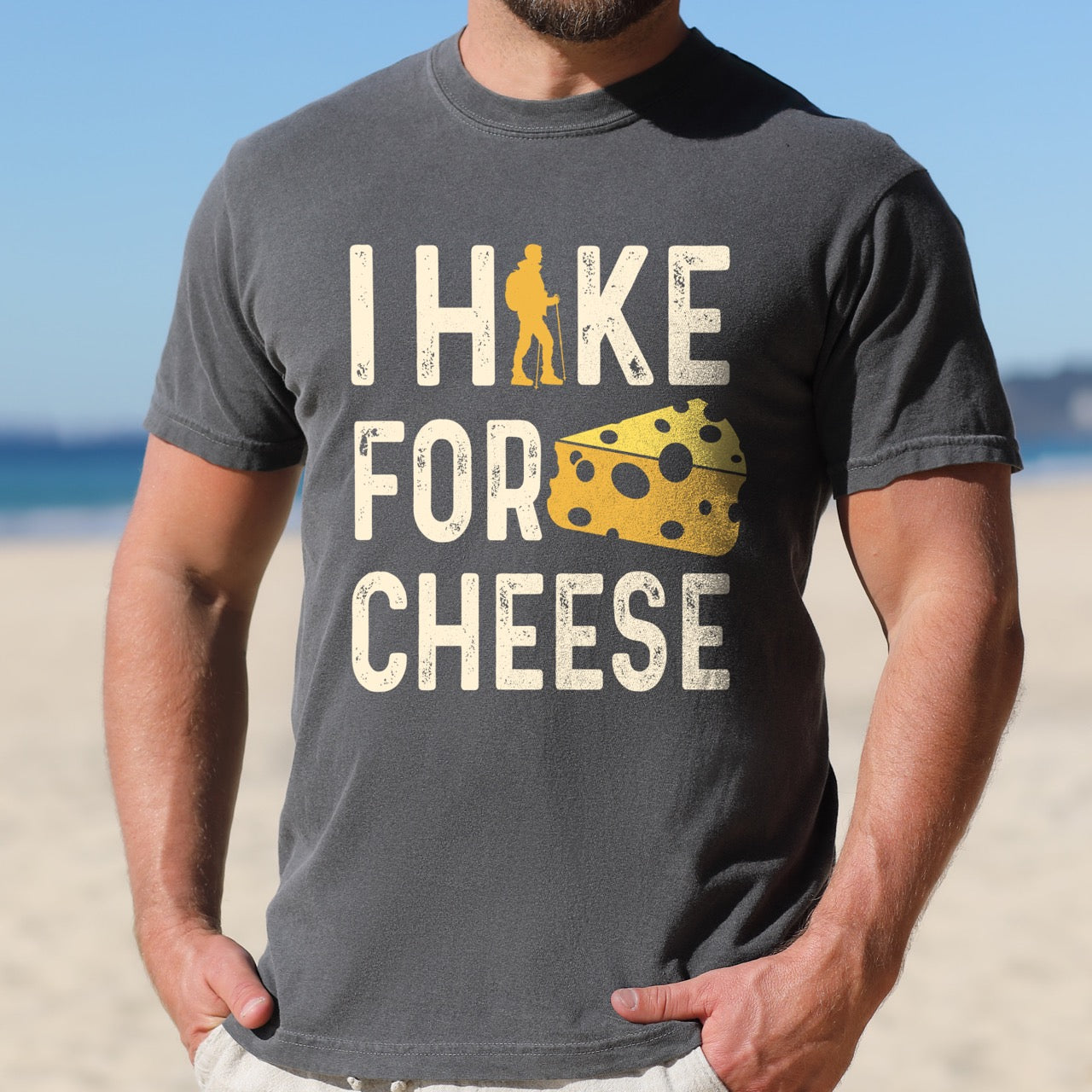Man wearing Pepper Cheese lover vintage tee I Hike for Cheese with distressed cream typography character silhouette with trekking pole and illustrated Swiss cheese wedge with holes on Comfort Colors shirt for dairy and food enthusiasts, hikers and foodies.