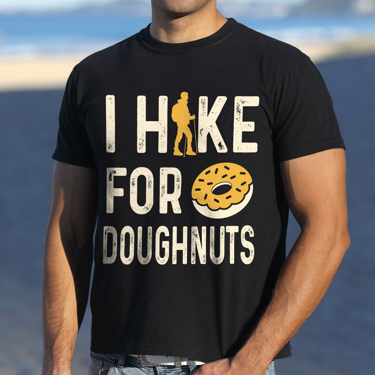 Man wearing black Doughnut donut lover statement tee I Hike for Doughnuts with vintage distressed cream typography character silhouette with trekking pole and illustrated glazed doughnut with sprinkles on Comfort Colors shirt for sweet treat enthusiasts, hikers and foodies.