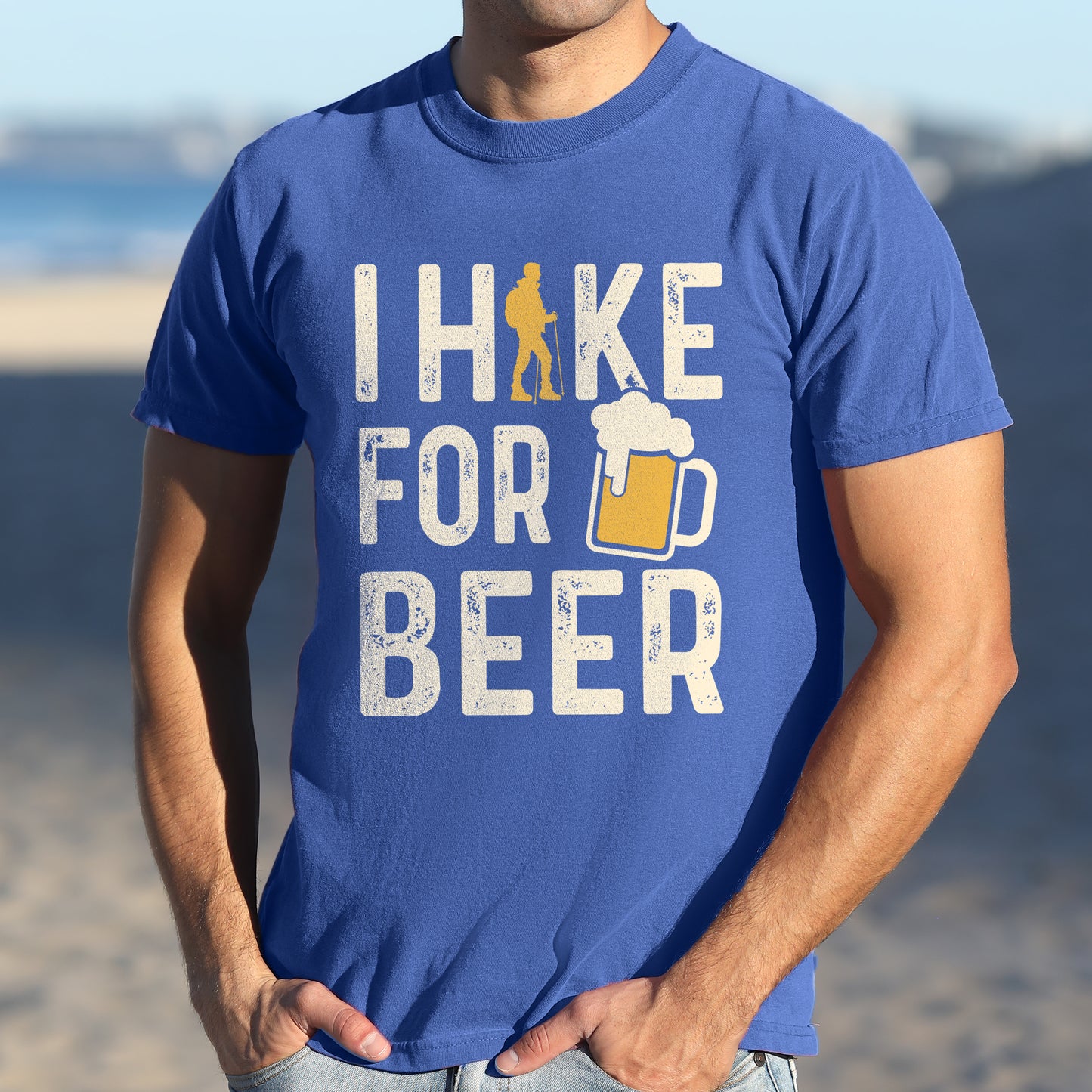 Flo Blue (Bright Blue) graphic t-shirt with 'I Hike for Beer' text in cream lettering featuring orange hiker silhouette and beer mug illustration with foam, styled with light wash jeans and brown hiking boots