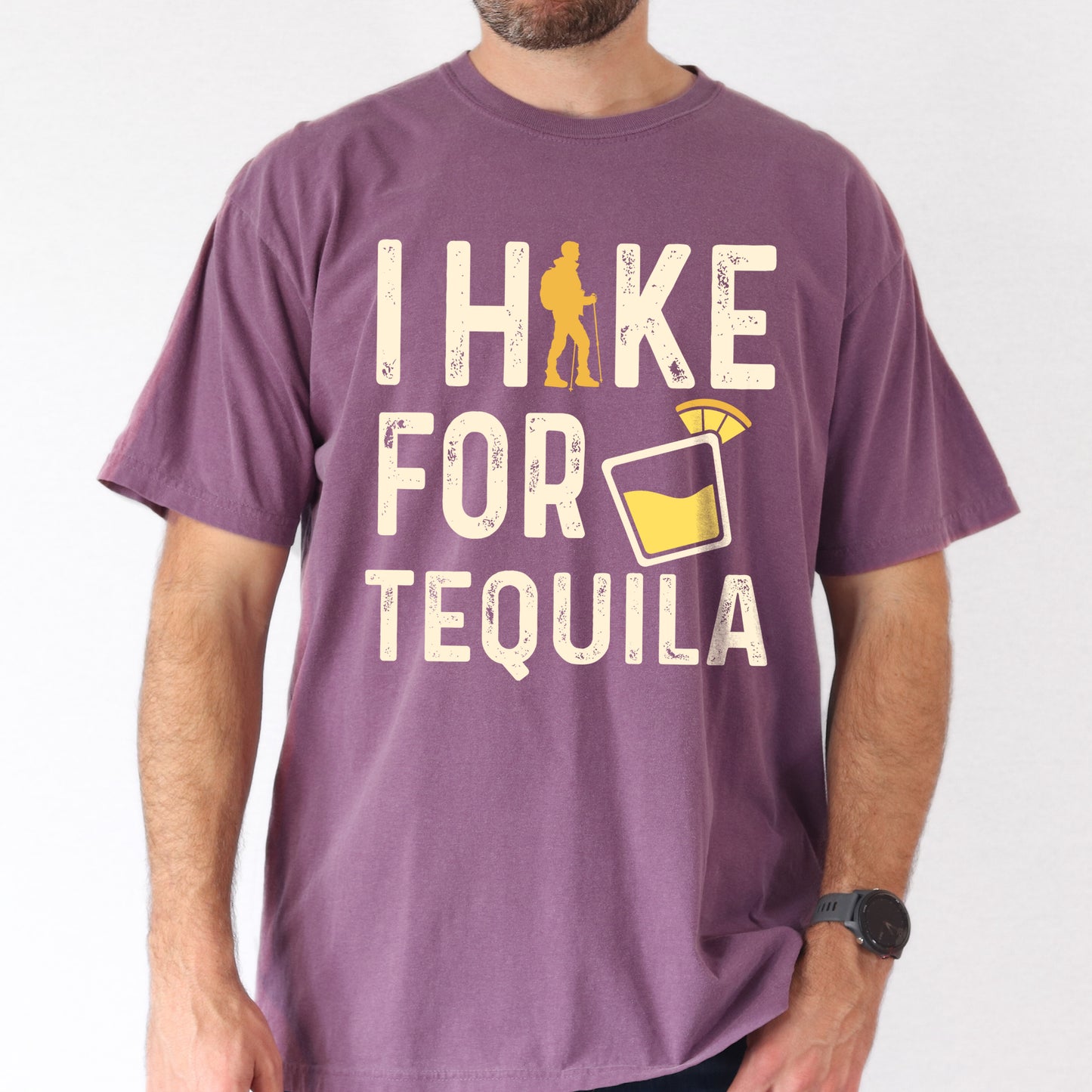 Berry (Dark Violet) graphic t-shirt with 'I Hike for Tequila' text in cream lettering featuring orange hiker silhouette and tequila shot glass illustration with lime garnish.