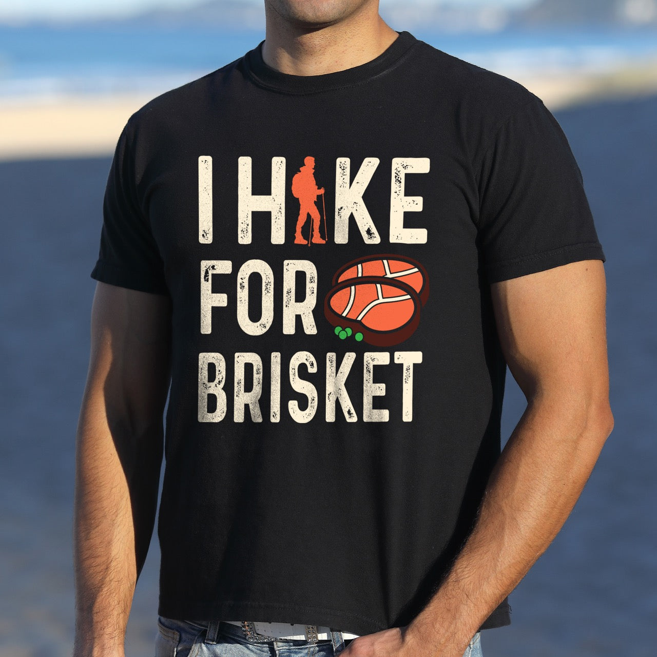Man wearing Black BBQ brisket lover statement tee I Hike for Brisket with distressed brown typography character silhouette with trekking pole and illustrated sliced smoked brisket with herb garnish on vintage Comfort Colors shirt for food motivated adventurers for hikers and foodies.