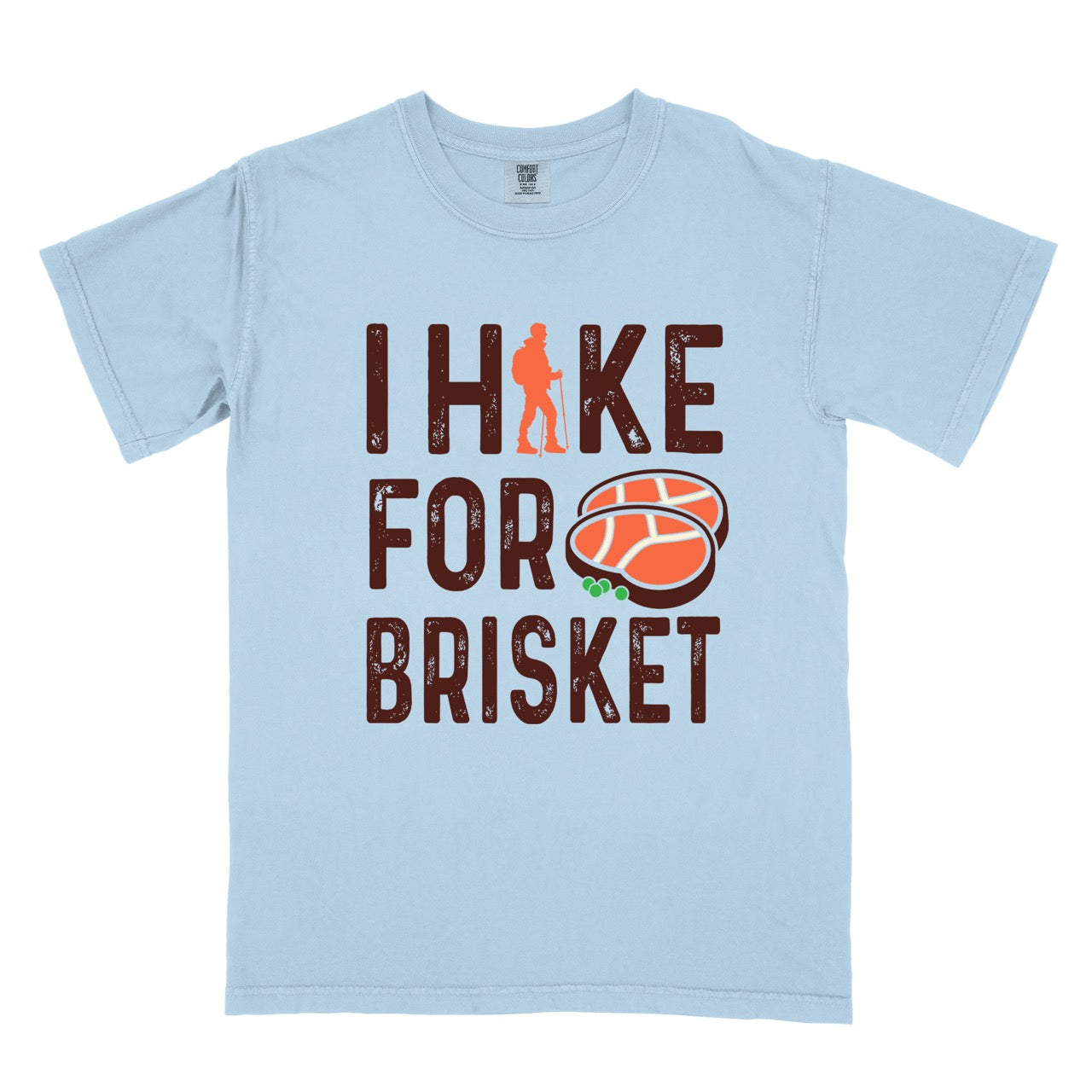 Chambray (light blue) BBQ brisket lover statement tee I Hike for Brisket with distressed brown typography character silhouette with trekking pole and illustrated sliced smoked brisket with herb garnish on vintage Comfort Colors shirt for food motivated adventurers for hikers and foodies.