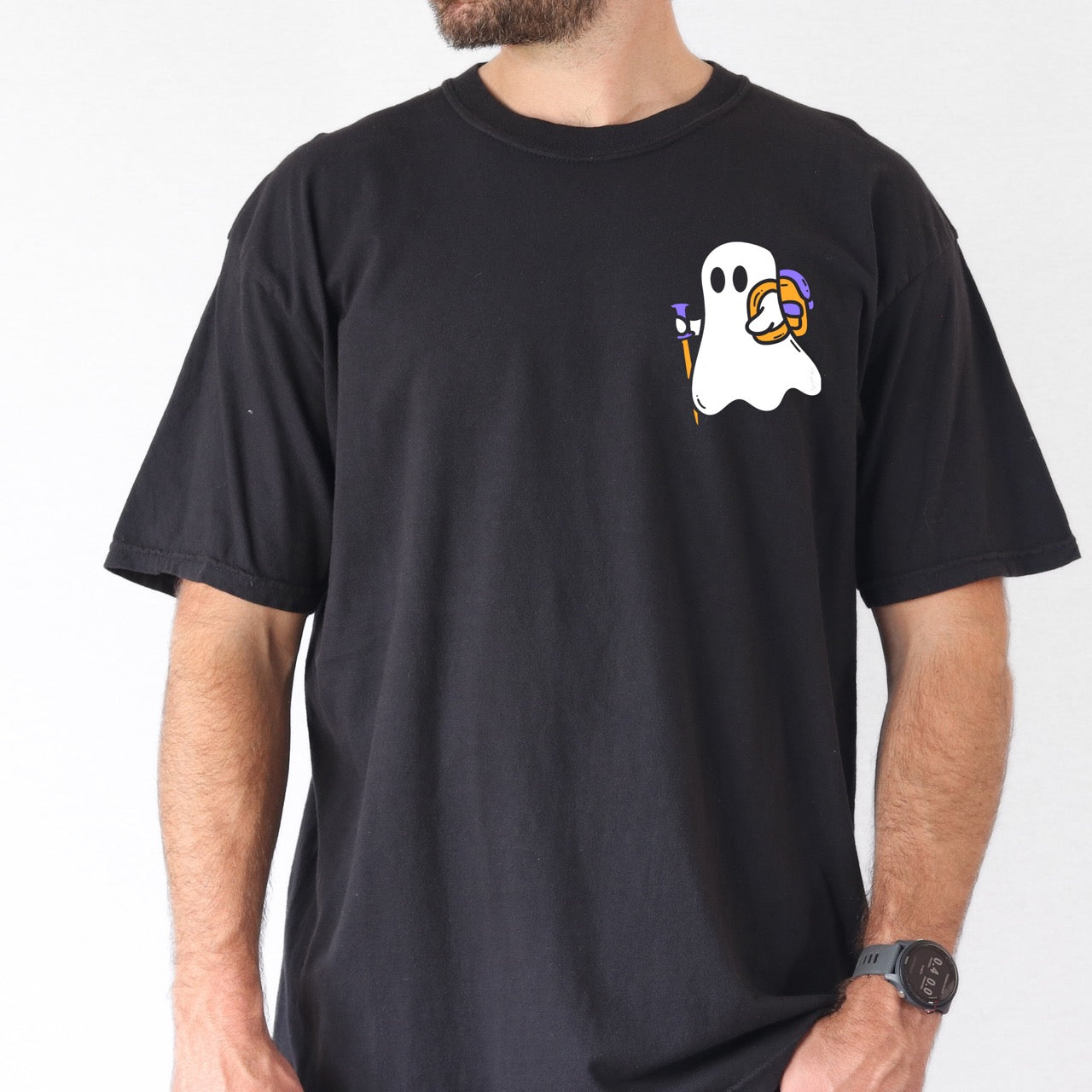 man wearing black Halloween ghost statement shirt featuring cute white Boo character with trekking pole and orange candy bucket filled with purple wrapped treats on chest placement Comfort Colors tee for spooky season celebrations for hikers and adventurers.