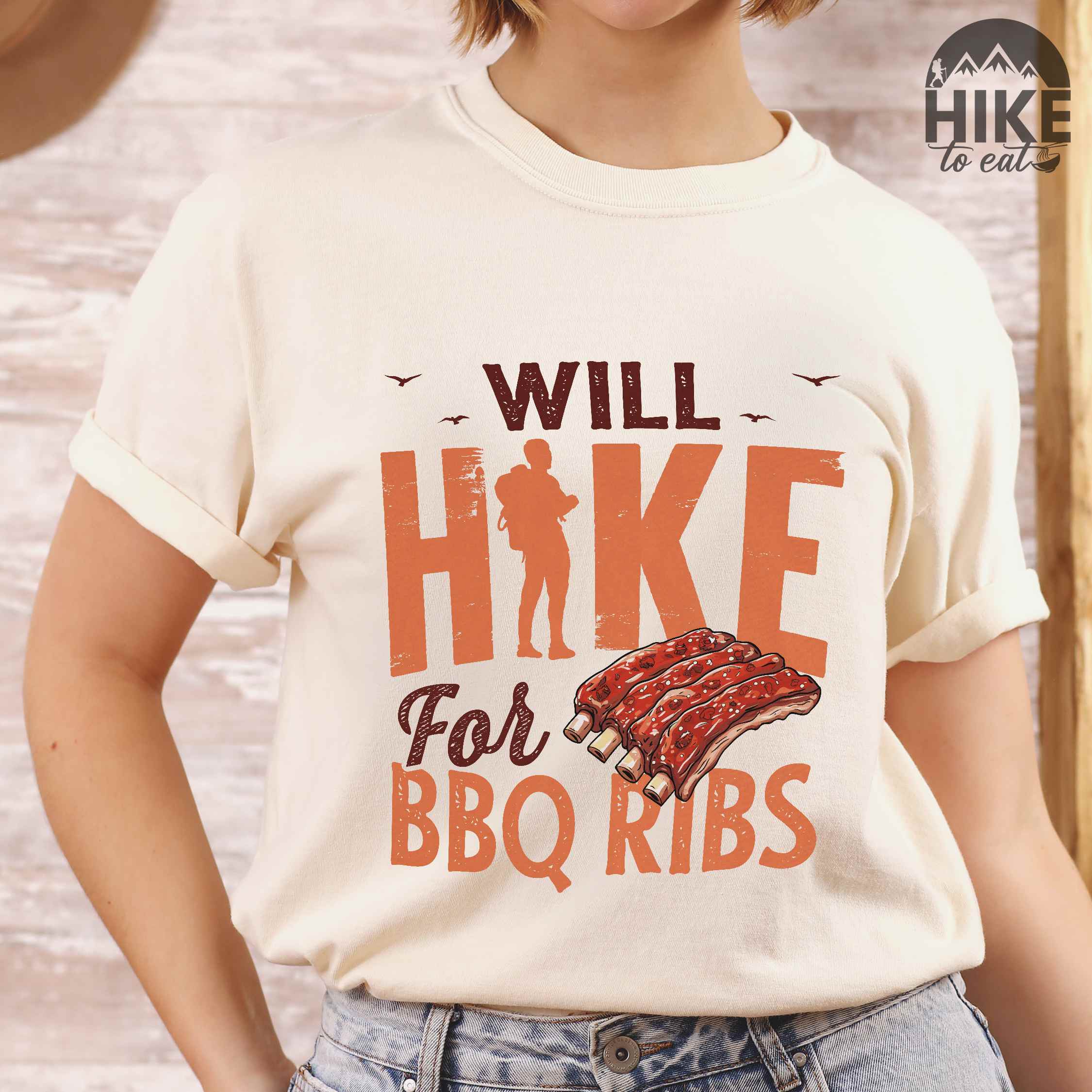 Woman wearing ivory "Will Hike for BBQ Ribs" colored vintage tee with bold typography, birds, juicy grilled bbq ribs illustration, and backpacker for bbq enthusiasts