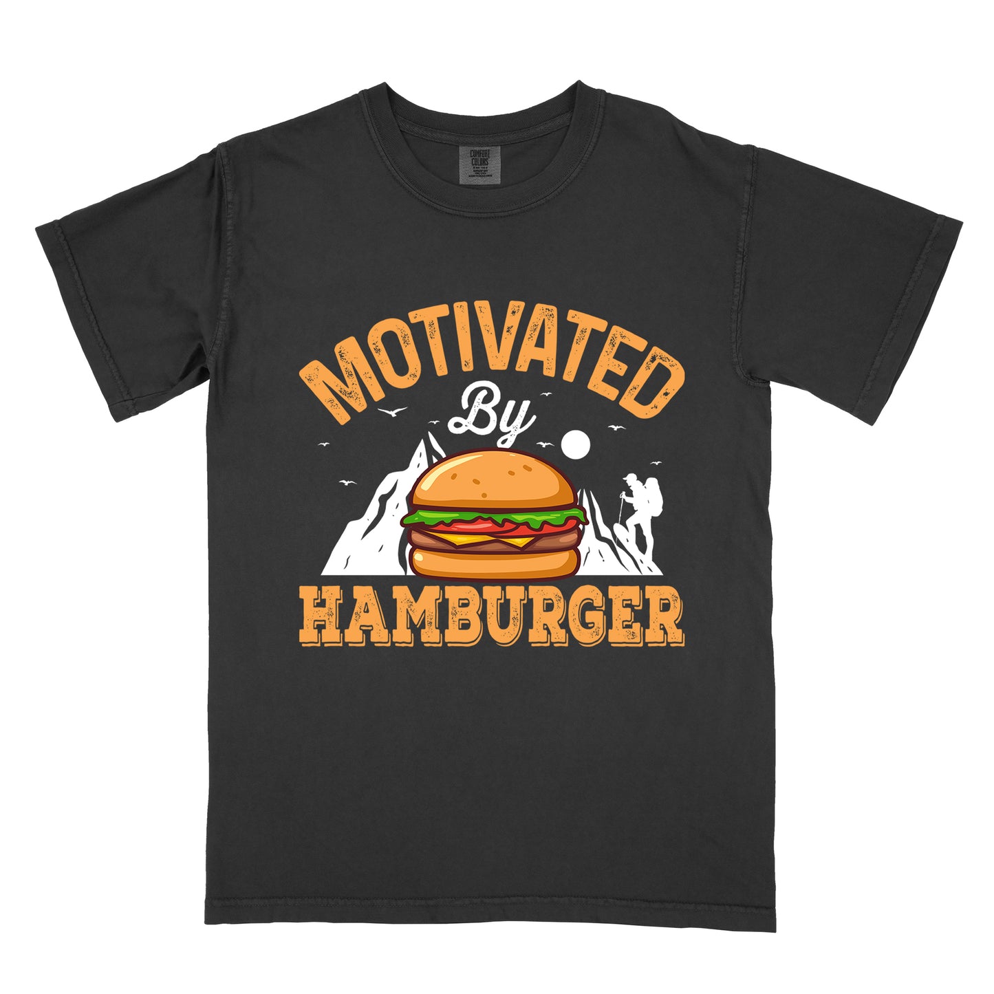 Black t-shirt with text "MOTIVATED By HAMBURGER". The word "MOTIVATED" appears in orange distressed letters at the top in an arc, "By" in white script in the middle, and "HAMBURGER" in matching orange at the bottom. The design features white mountain silhouettes with a small hiker figure, flying birds, and a sun or moon. A colorful hamburger illustration with bun, patty, cheese, lettuce and tomato sits in the center of the design.