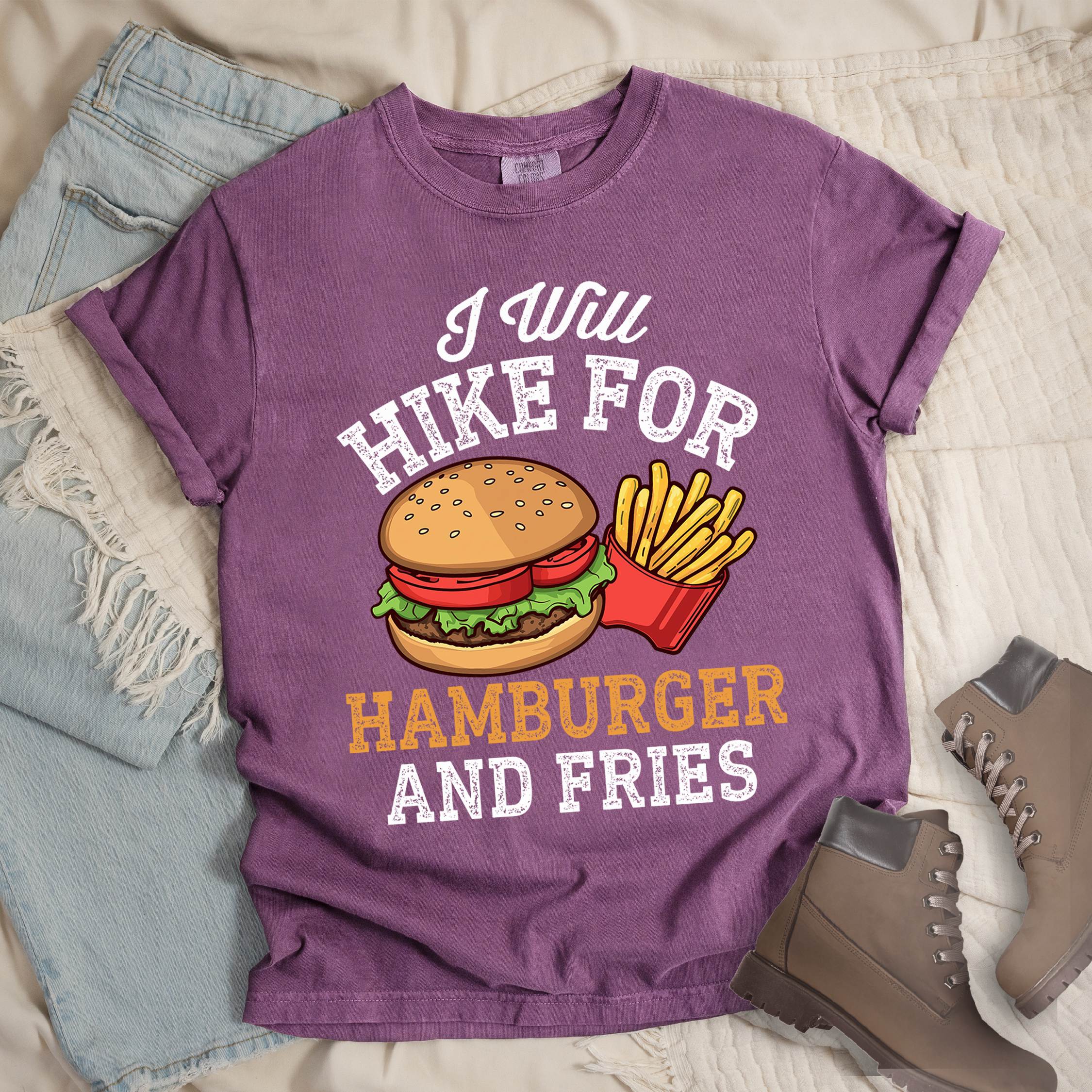 Dark pink t-shirt with distressed text reading "I Will HIKE FOR HAMBURGER AND FRIES". The words "I Will" appear in script at the top, "HIKE FOR" in white block letters, "HAMBURGER" in gold/orange, and "AND FRIES" in white at the bottom. Center illustration shows a detailed hamburger with bun, patty, lettuce, and tomato next to a red container of yellow french fries.