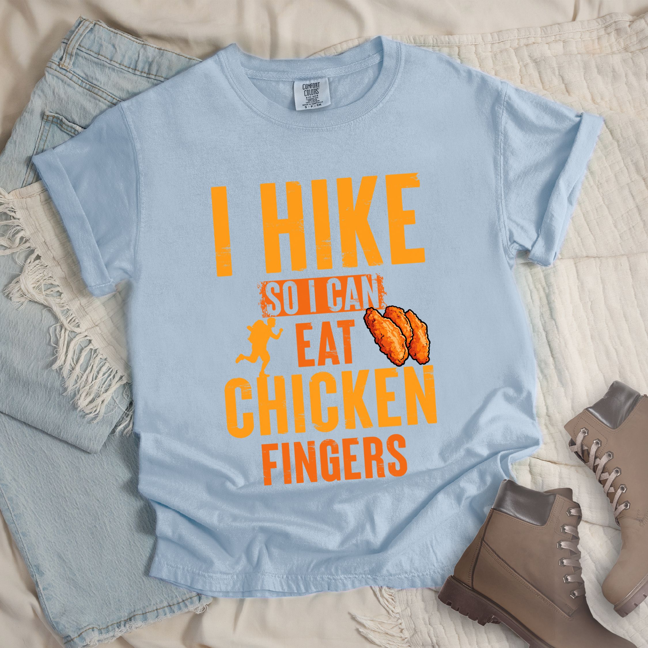 Light blue shirt with Hiking Design featuring the phrase “I Hike So I Can Eat Chicken Fingers” and an illustration of crispy chicken fingers beside a hiker silhouette.