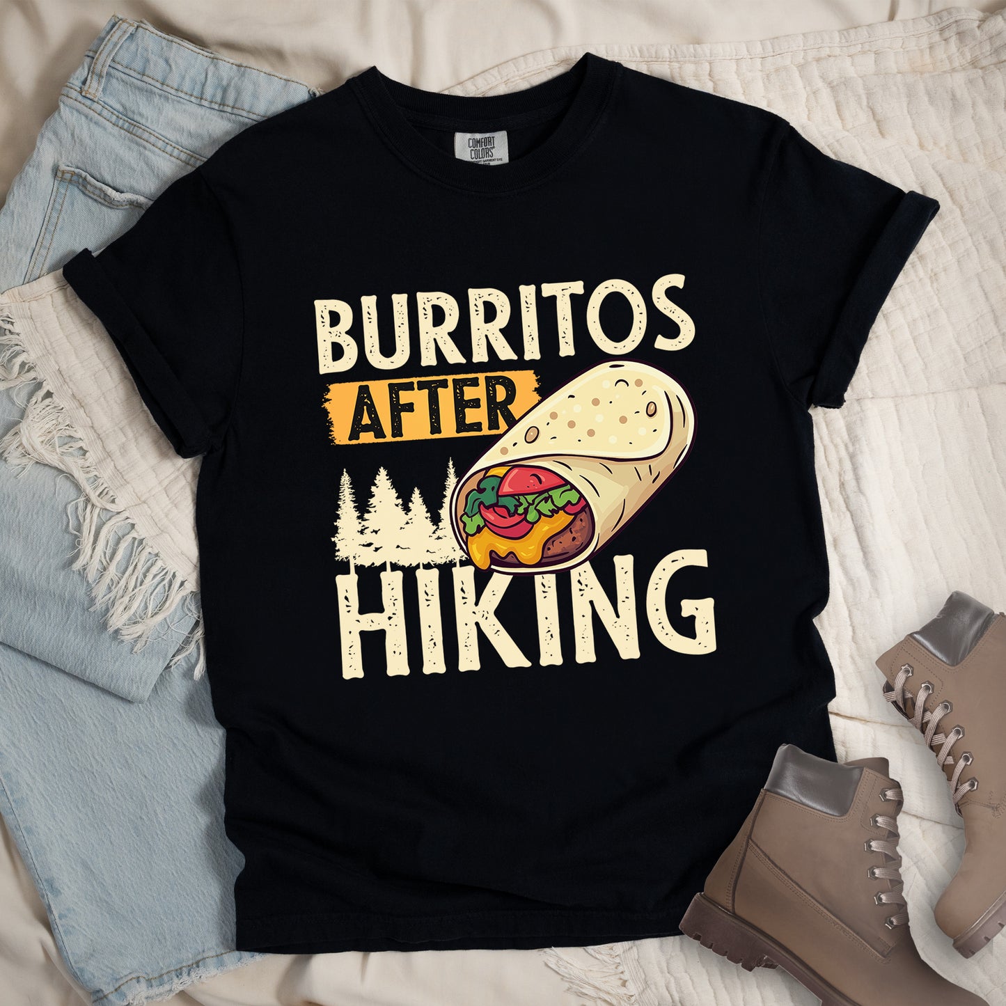 Black t-shirt with distressed text reading "BURRITOS AFTER HIKING". "BURRITOS" appears at the top in cream/off-white letters, "AFTER" in black text on an orange background in the middle, and "HIKING" in matching cream letters at the bottom. Between the text is an illustration of a burrito with visible fillings (beans, cheese, lettuce, tomato) and pine tree silhouettes in cream color. The design has a vintage, weathered appearance.