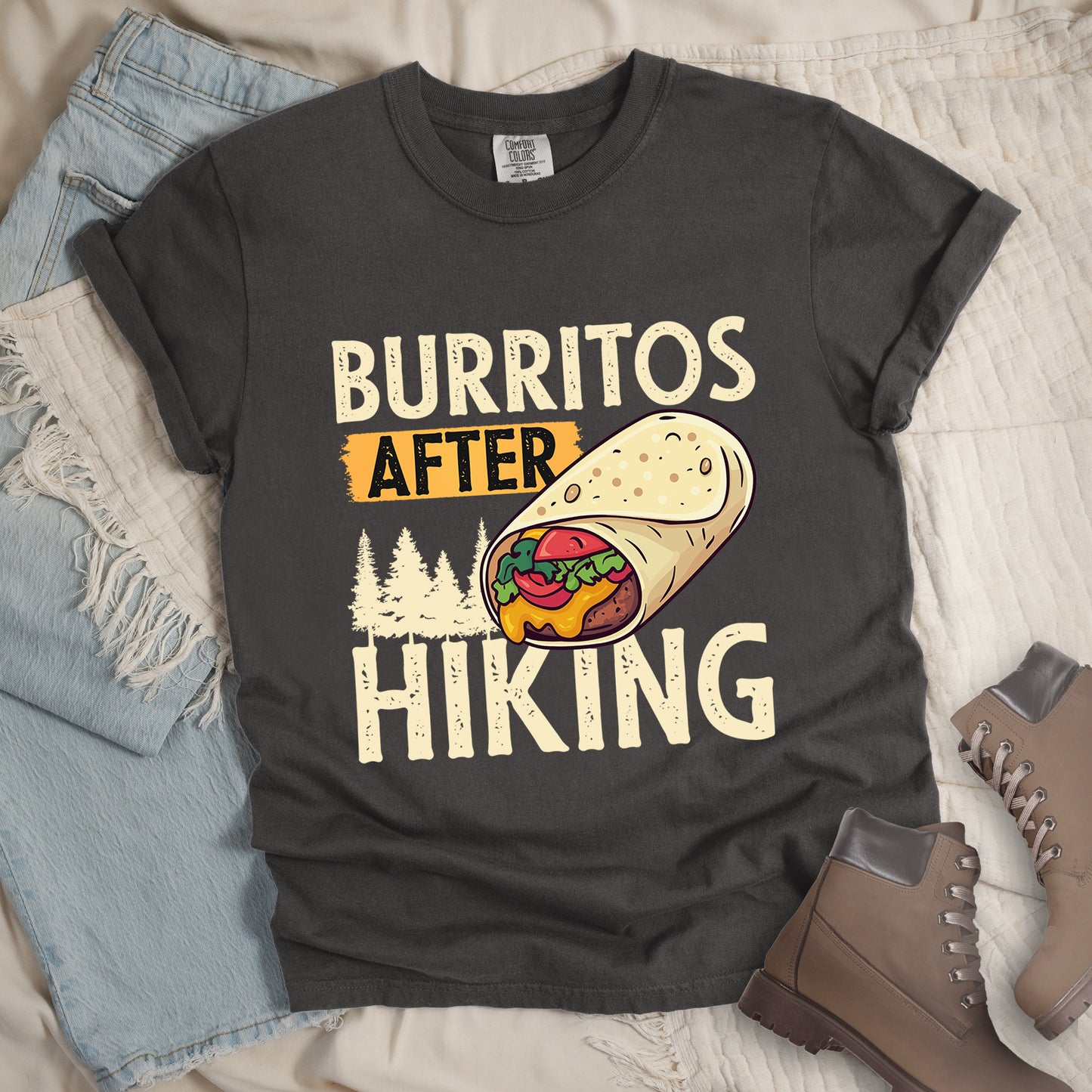 Pepper (Dark Gray) t-shirt with distressed text reading "BURRITOS AFTER HIKING". "BURRITOS" appears at the top in cream/off-white letters, "AFTER" in black text on an orange background in the middle, and "HIKING" in matching cream letters at the bottom. Between the text is an illustration of a burrito with visible fillings (beans, cheese, lettuce, tomato) and pine tree silhouettes in cream color. The design has a vintage, weathered appearance.
