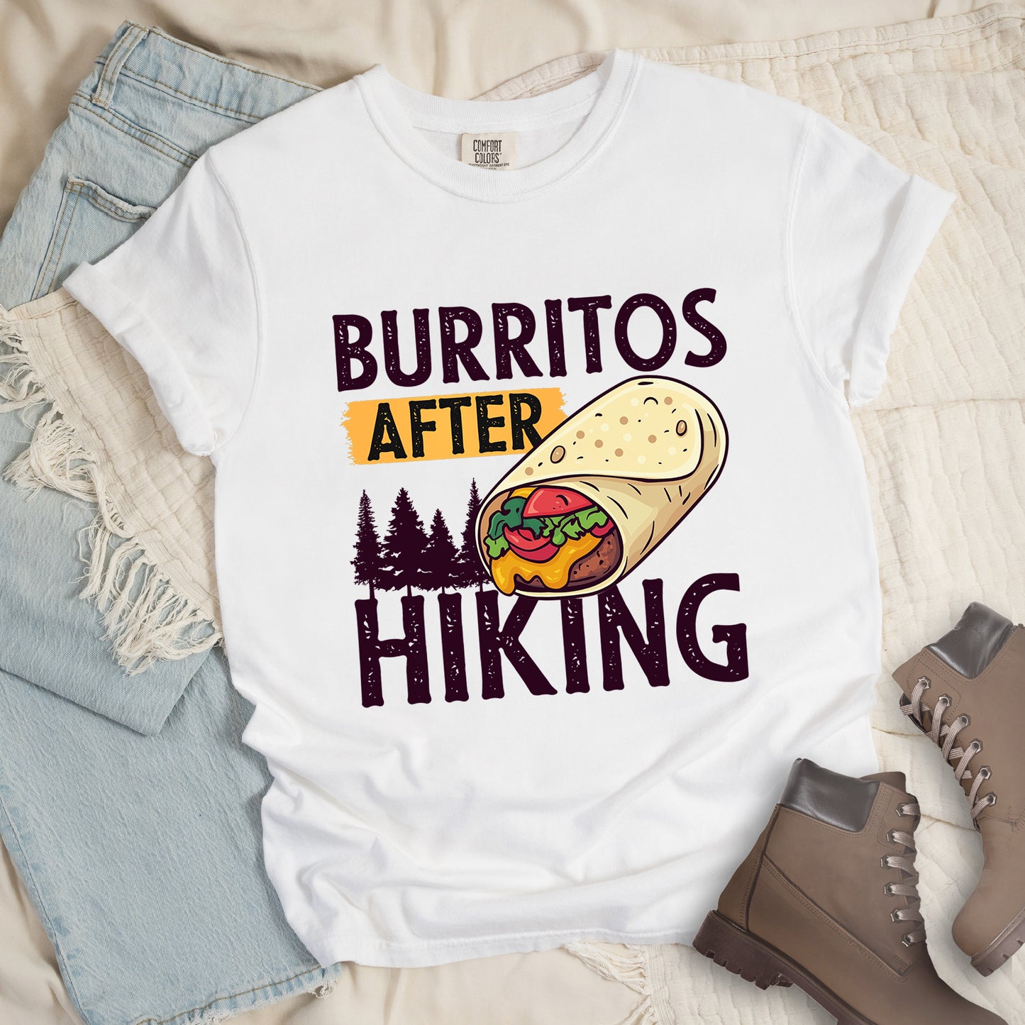 White t-shirt with distressed text reading "BURRITOS AFTER HIKING". "BURRITOS" appears at the top in deep violet letters, "AFTER" in black text on an orange background in the middle, and "HIKING" in matching deep violet letters at the bottom. Between the text is an illustration of a burrito with visible fillings (beans, cheese, lettuce, tomato) and pine tree silhouettes in deep violet color. The design has a vintage, weathered appearance.
