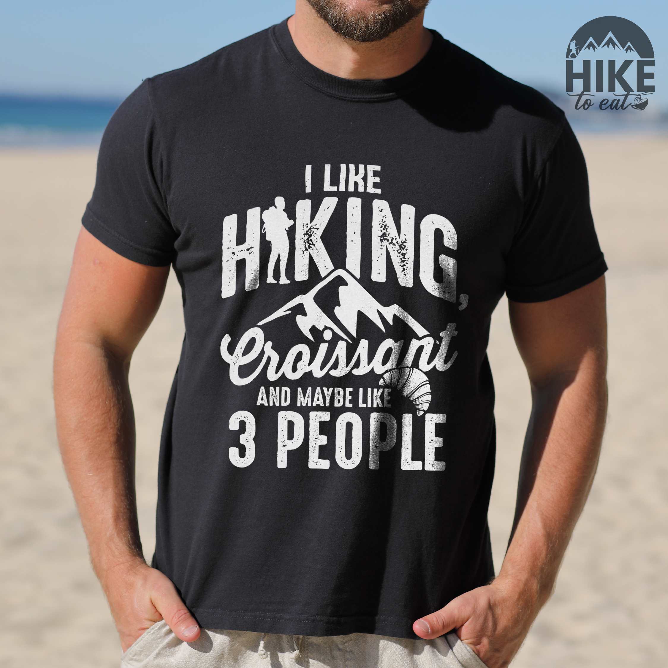 Man wearing black "I Like hiking, croissant and maybe like 3 people" colored vintage tee with bold typography, birds, mountains, illustrated croissant, and backpacker for pastry enthusiasts.