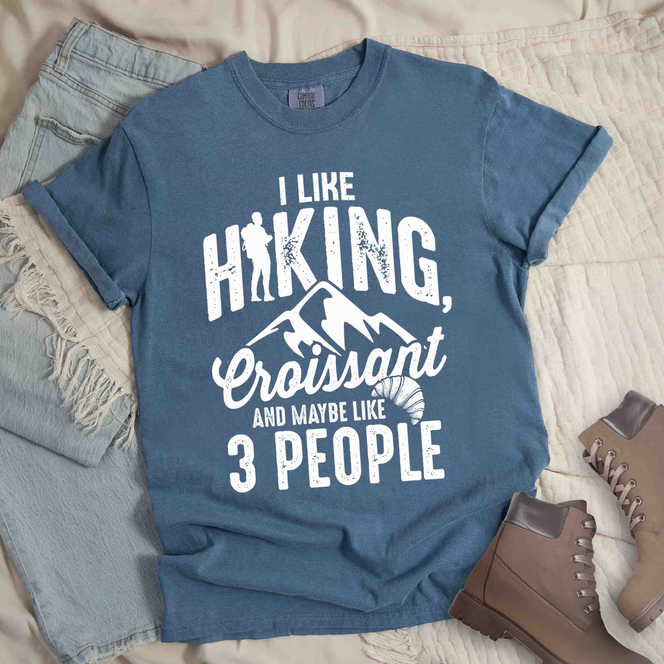 blue jean "I Like hiking, croissant and maybe like 3 people" colored vintage tee with bold typography, birds, mountains, illustrated croissant, and backpacker for pastry enthusiasts.