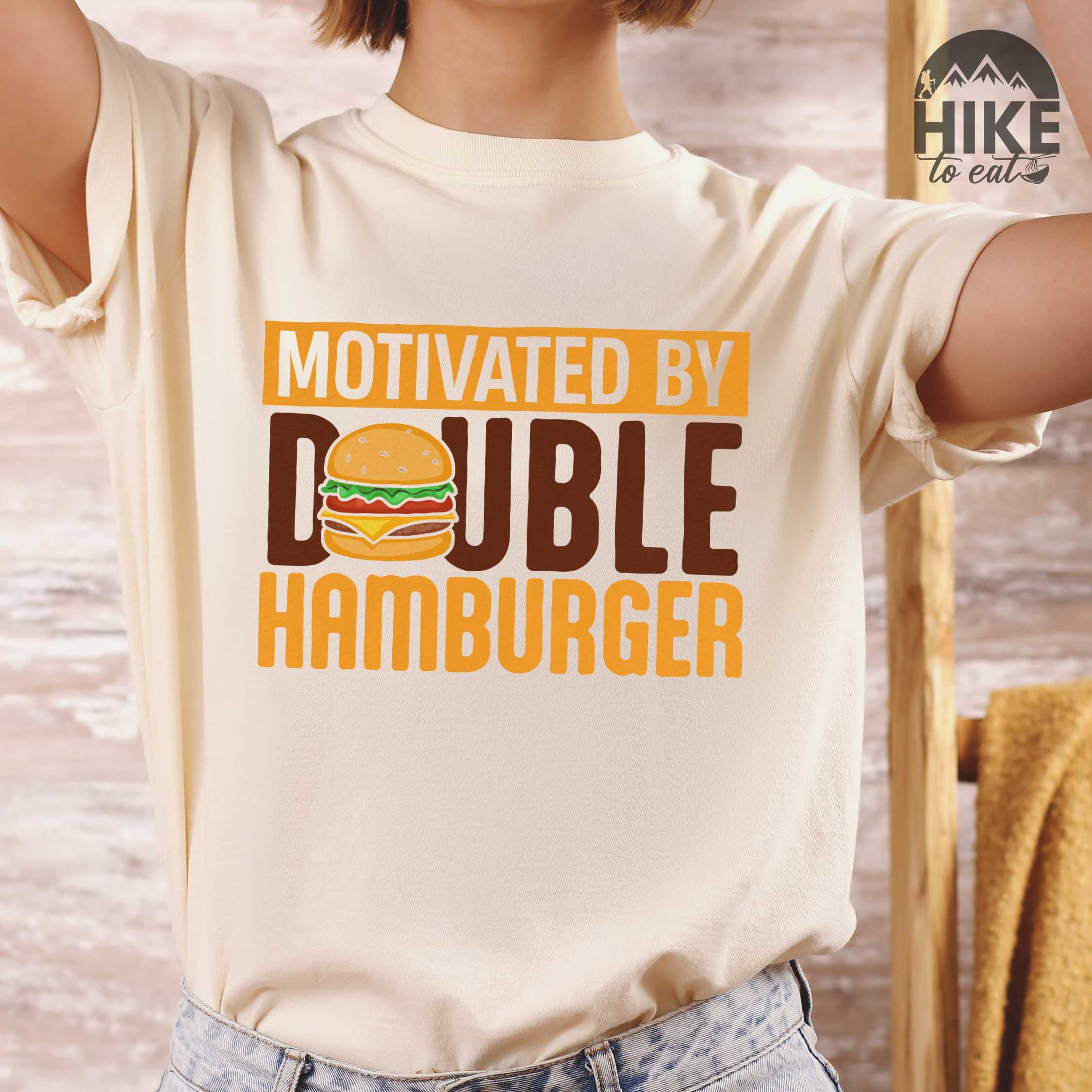 Woman wearing ivory "Motivated by Double Hamburger" colored vintage tee with bold typography, illustrated juicy hamburger, and backpacker for burger enthusiasts.