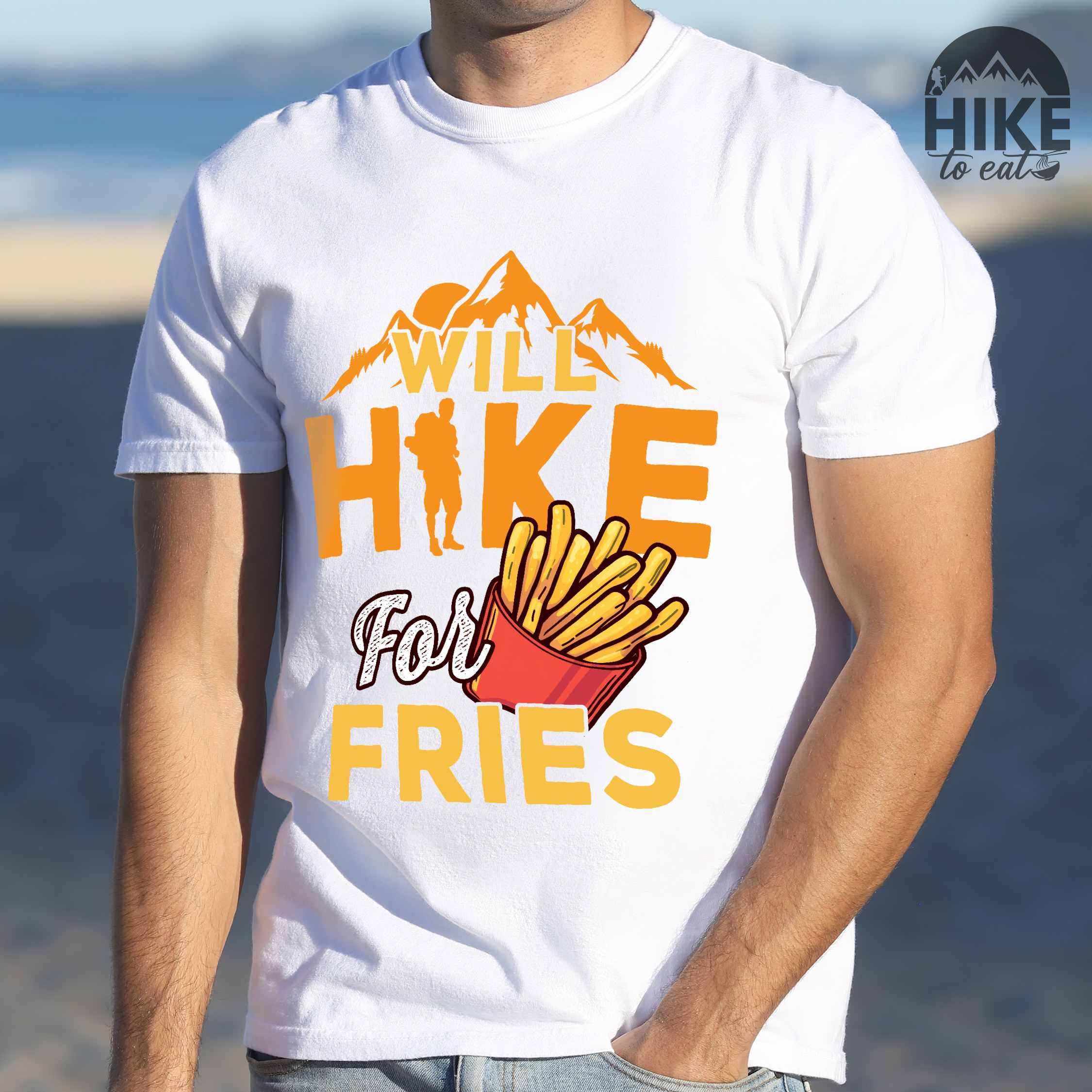 Man wearing white "Will Hike for Fries" colored vintage tee with bold typography, mountains, illustrated fries, and backpacker for comfort food enthusiasts.