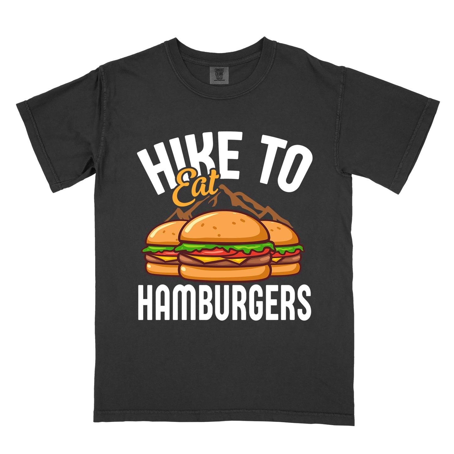 Black t-shirt with text "HIKE TO Eat HAMBURGERS". "HIKE TO" appears in white arched letters at the top, "Eat" in orange script in the middle, and "HAMBURGERS" in white at the bottom. The center features an illustration of three hamburgers with buns, lettuce, tomato, cheese and beef patties, with brown mountain silhouettes behind them. The design connects hiking activity with food rewards.