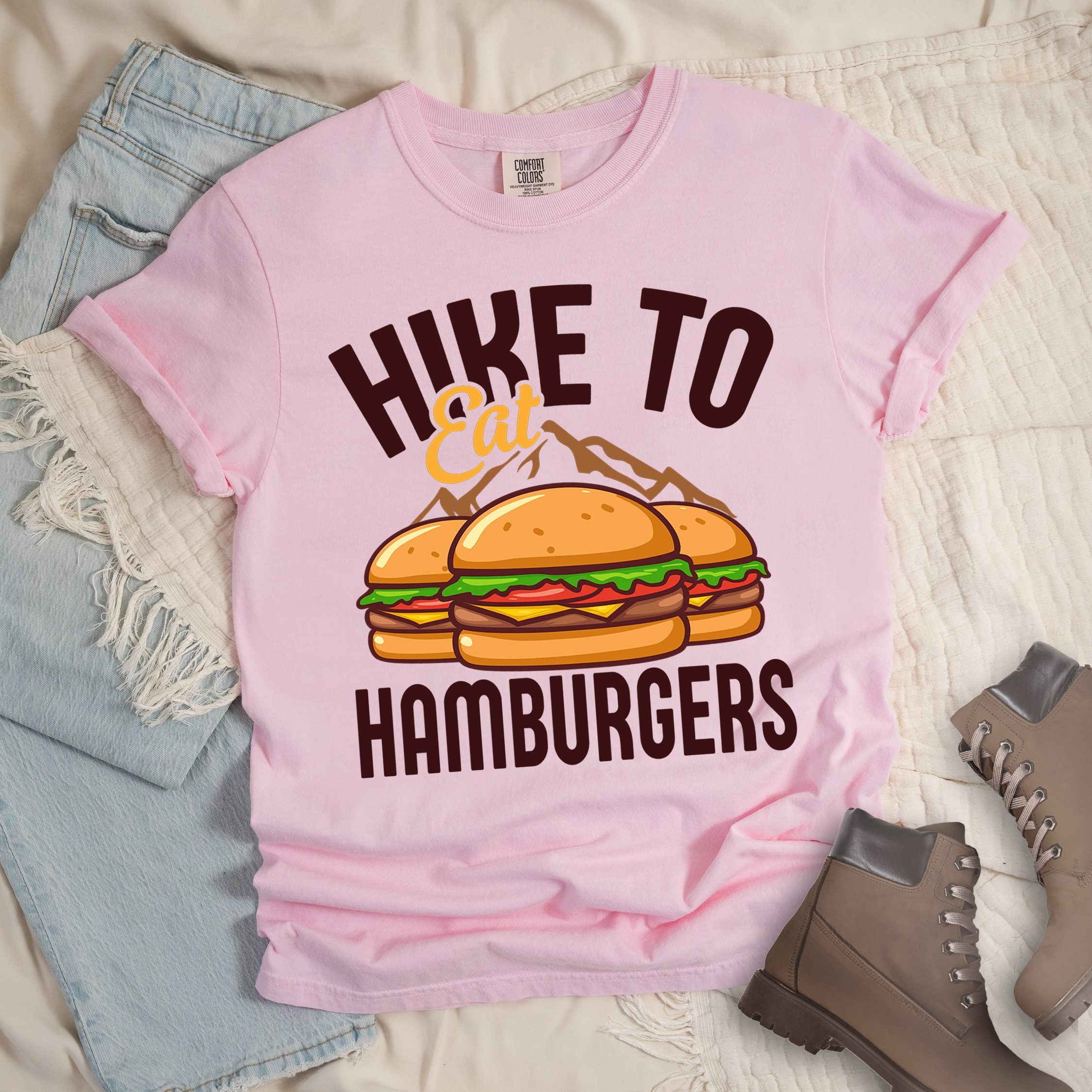 Light pink shirt with Hiking Design featuring the phrase “Hike to Eat Hamburgers” and an illustration of two hamburgers placed in front of mountain outlines.