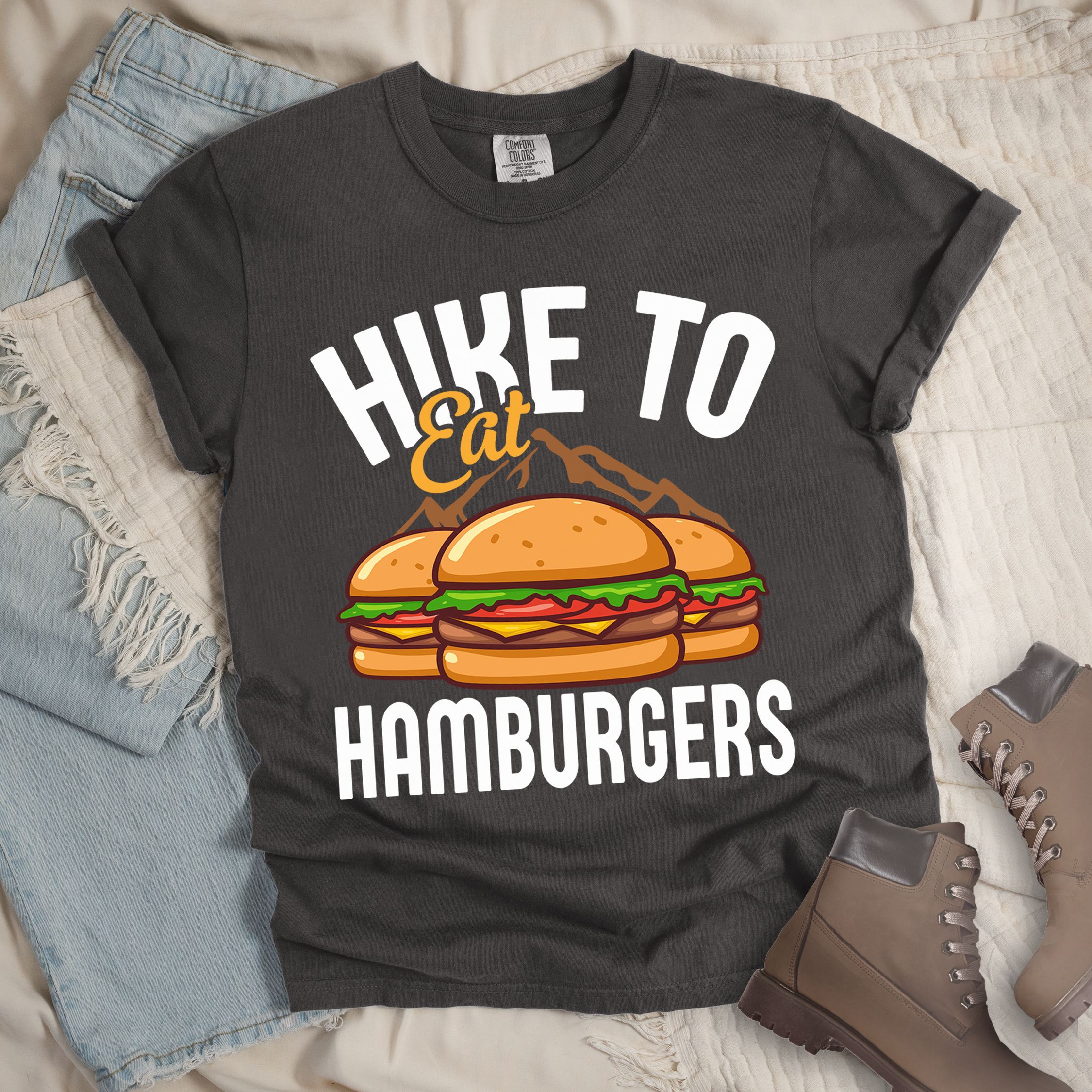 Dark grey shirt with Hiking Design featuring the phrase “Hike to Eat Hamburgers” and an illustration of two hamburgers placed in front of mountain outlines.