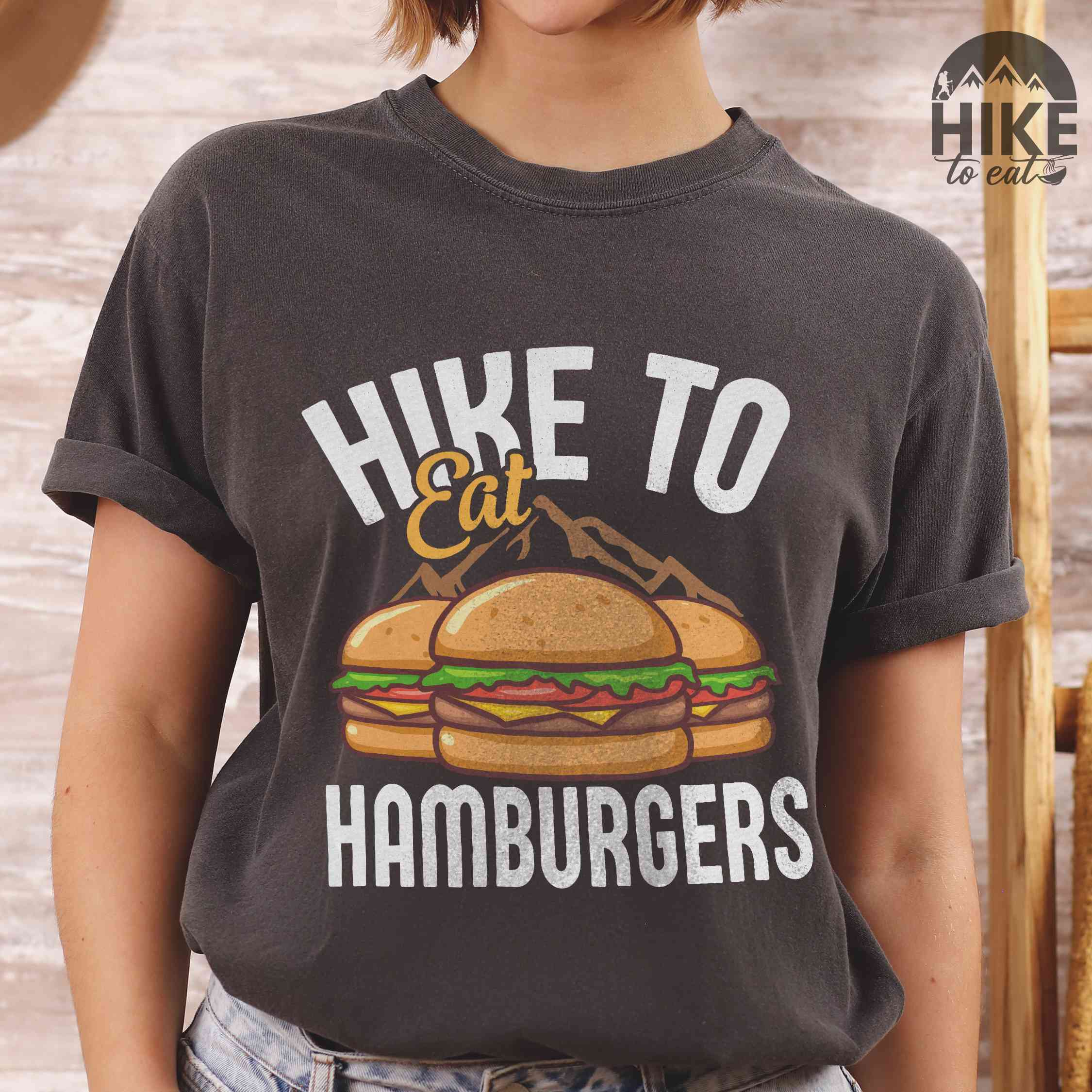 Woman wearing pepper "Hike to Eat Hamburgers" colored vintage tee with bold typography, illustrated juicy hamburger, and backpacker for burger enthusiasts.