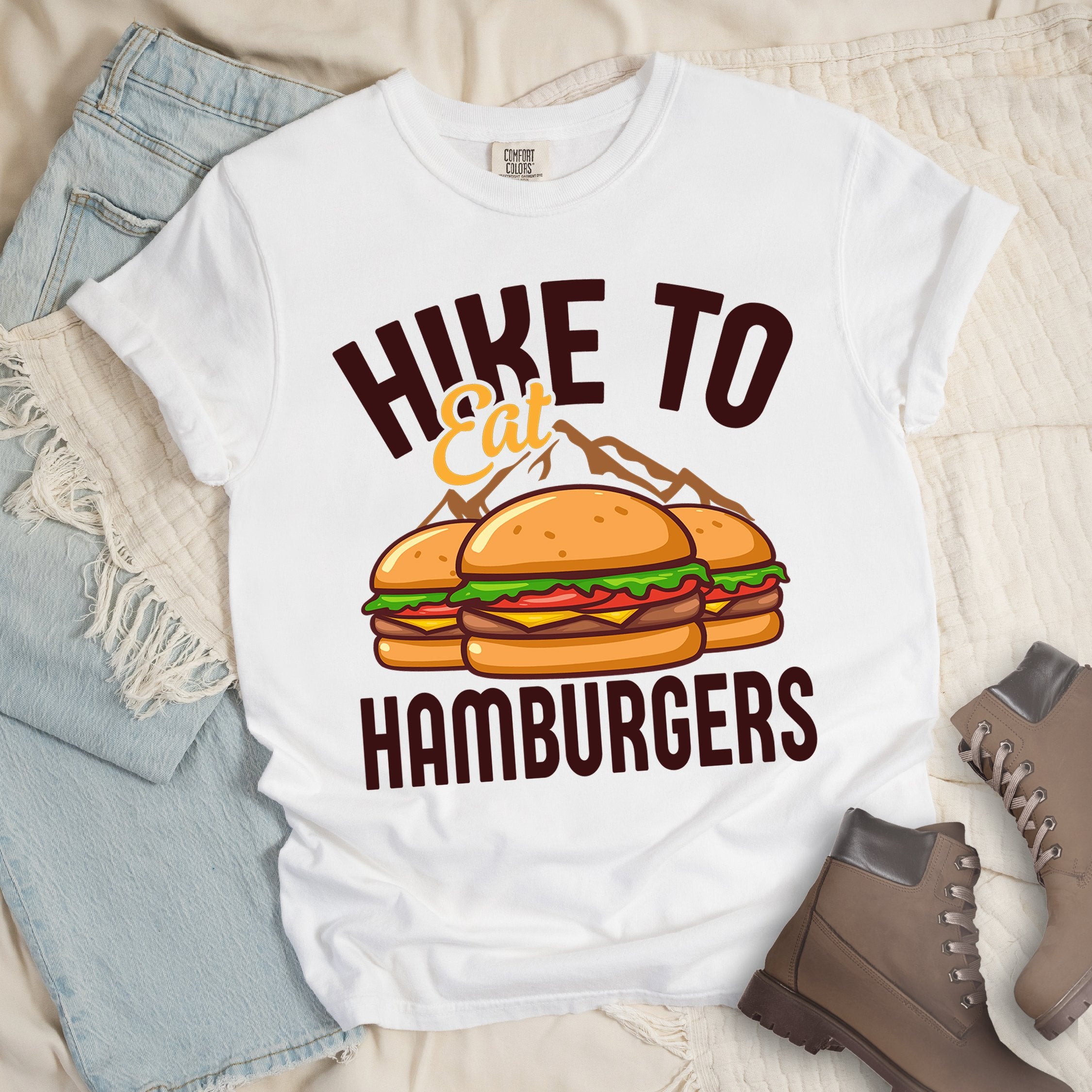 White shirt with Hiking Design featuring the phrase “Hike to Eat Hamburgers” and an illustration of two hamburgers placed in front of mountain outlines.