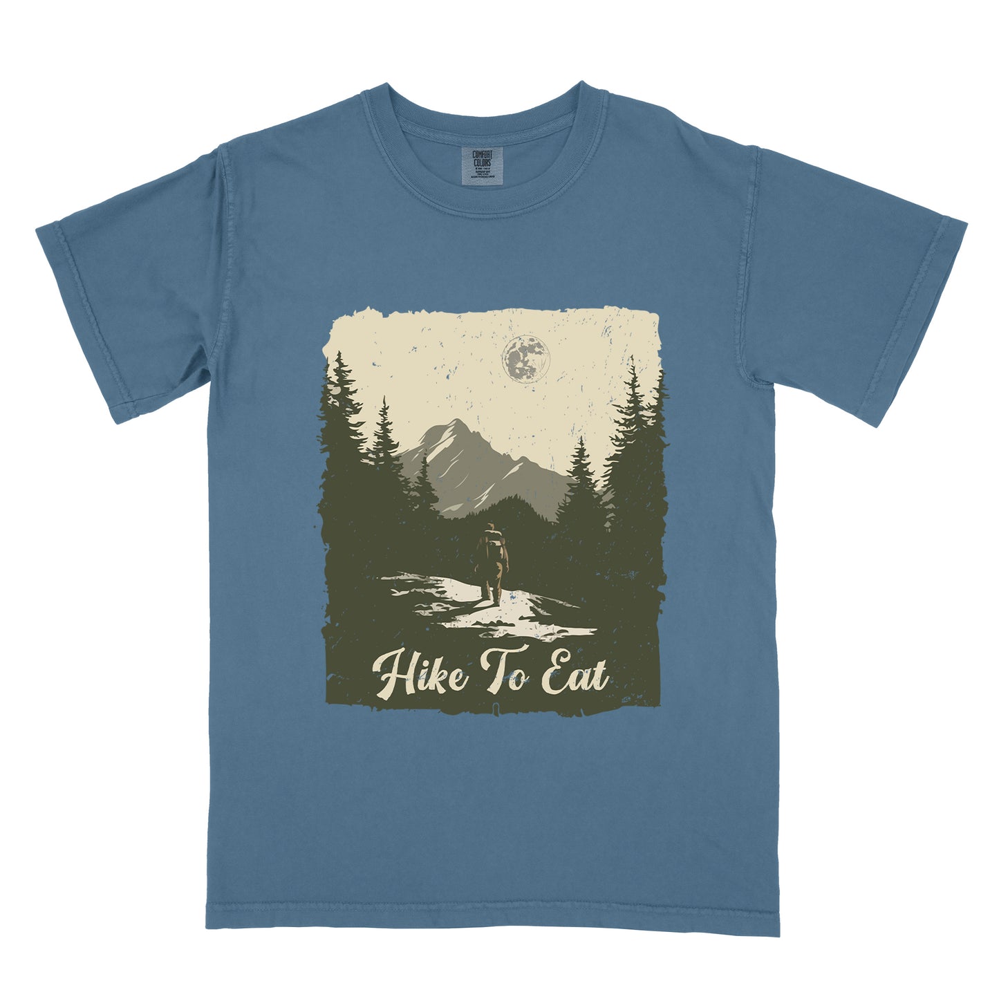 Blue Jean (Denim Blue) t-shirt featuring a vintage-style illustration of a lone hiker on a mountain trail. The rectangular design shows pine trees, mountain silhouettes, and a full moon against a cream-colored sky. A solitary hiker with backpack stands on the path facing the mountains. "Hike To Eat" appears in cream script at the bottom of the illustration. The artwork uses muted green, cream, and gray tones in a distressed, rustic style.