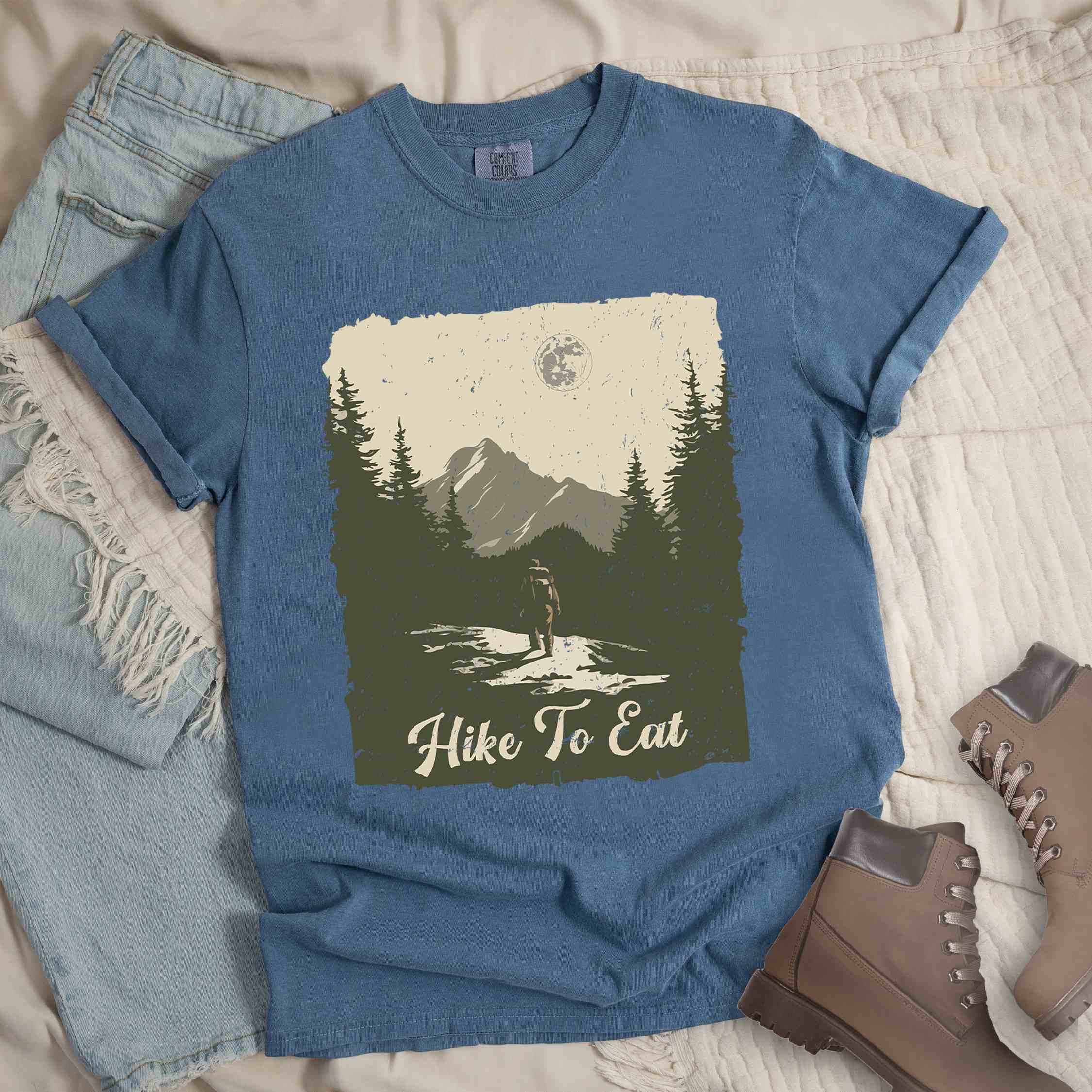 Blue jean "Hike to Eat" colored vintage tee with bold typography, illustrated landscape, and backpacker for burger enthusiasts.